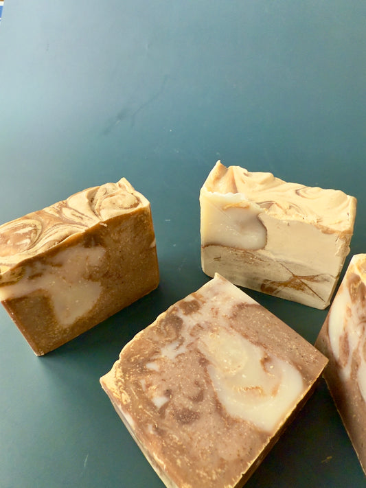 Three marbled soap bars on a green surface. Banana Almond soap bar with a warm tan marbled look and natural banana powder texture.