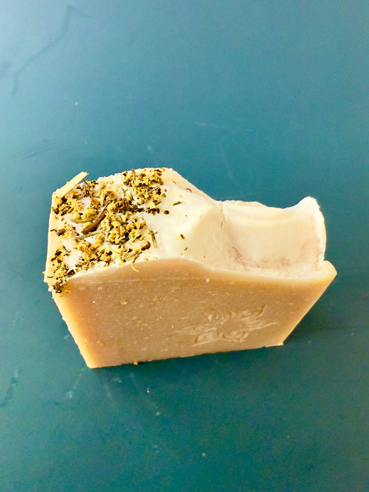 Handcrafted pear-inspired soap with blush tones and elder flowers on top, photographed on a teal background.