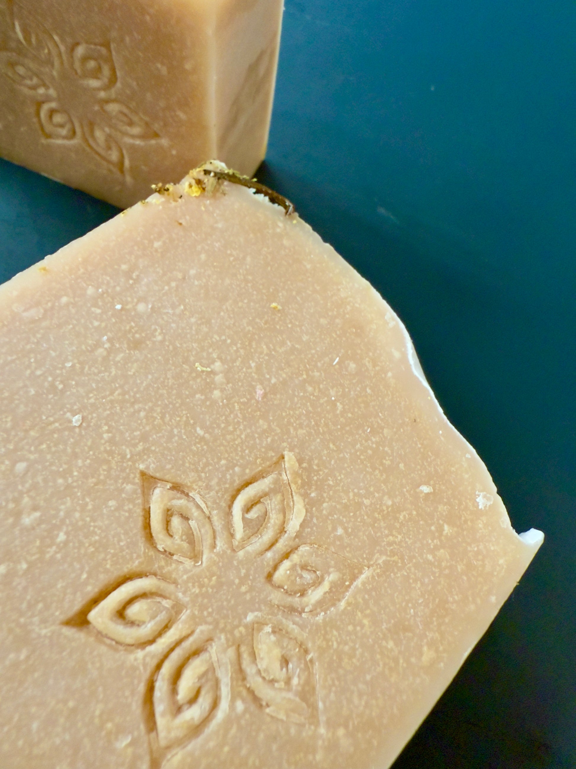 Close-up of a bar of soap with an embossed design on a blue background. Handcrafted pear-inspired soap with blush tones and elder flowers on top.
