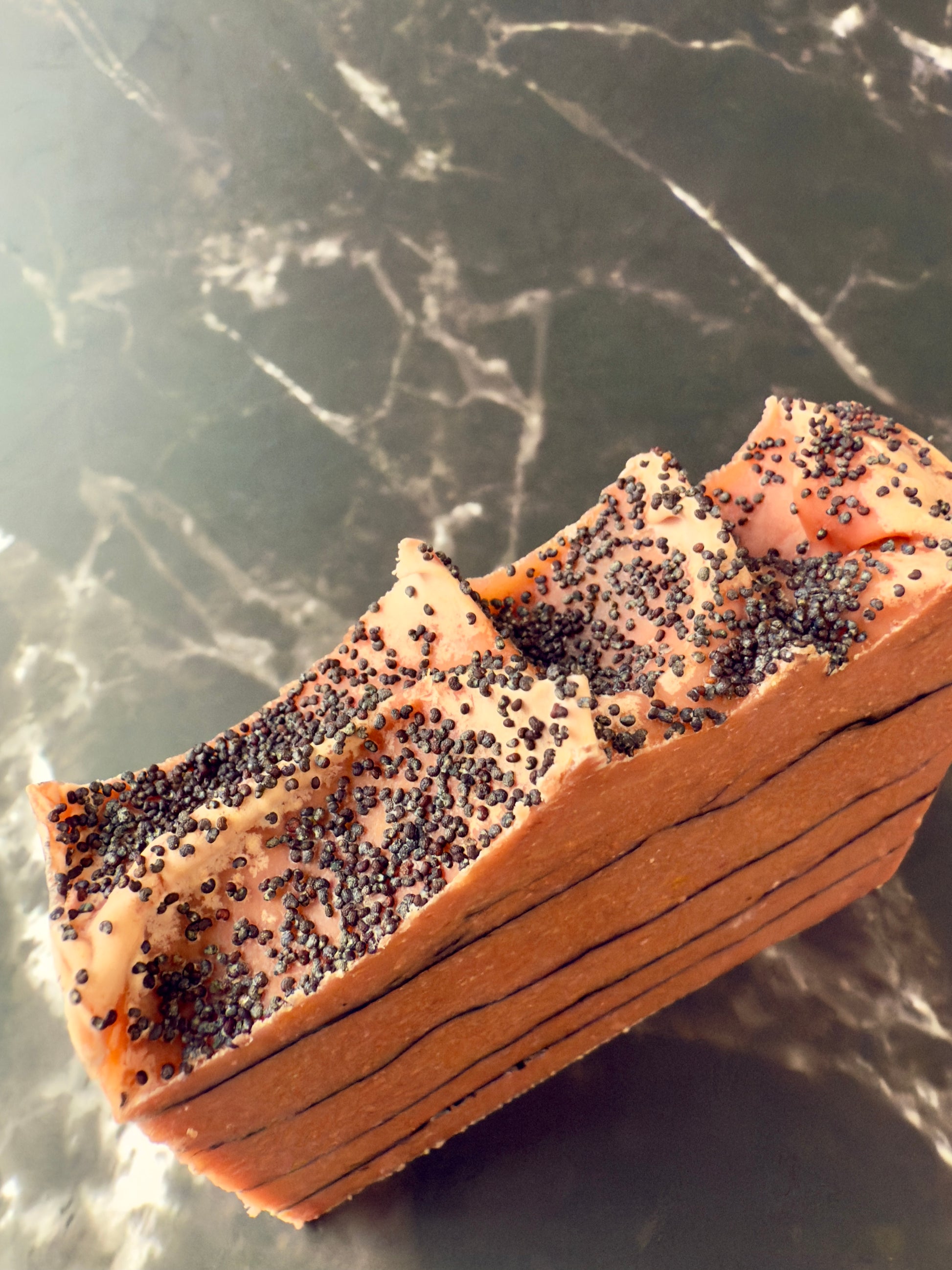Brick-red Tomato cold process soap with black charcoal pencil lines and poppy-seed top, displayed on dark marble.