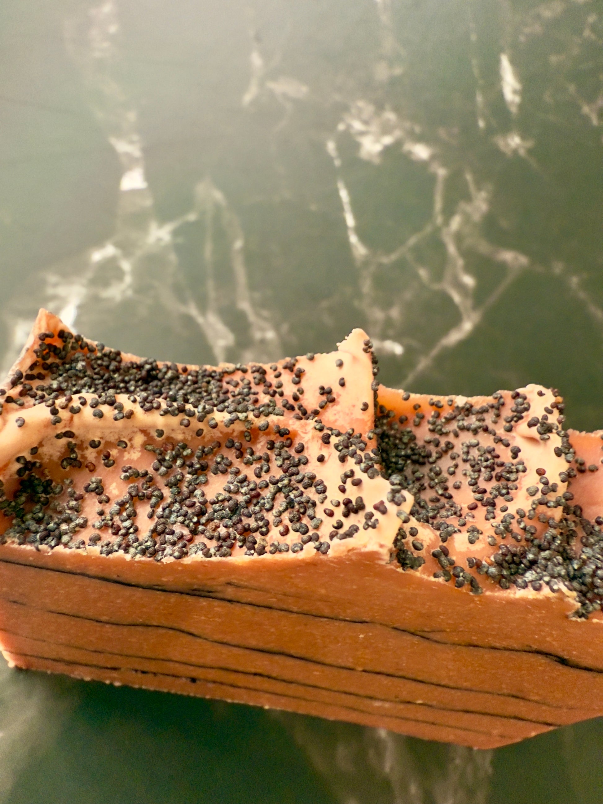 Brick-red Tomato cold process soap with black charcoal pencil lines and poppy-seed top, displayed on dark marble.