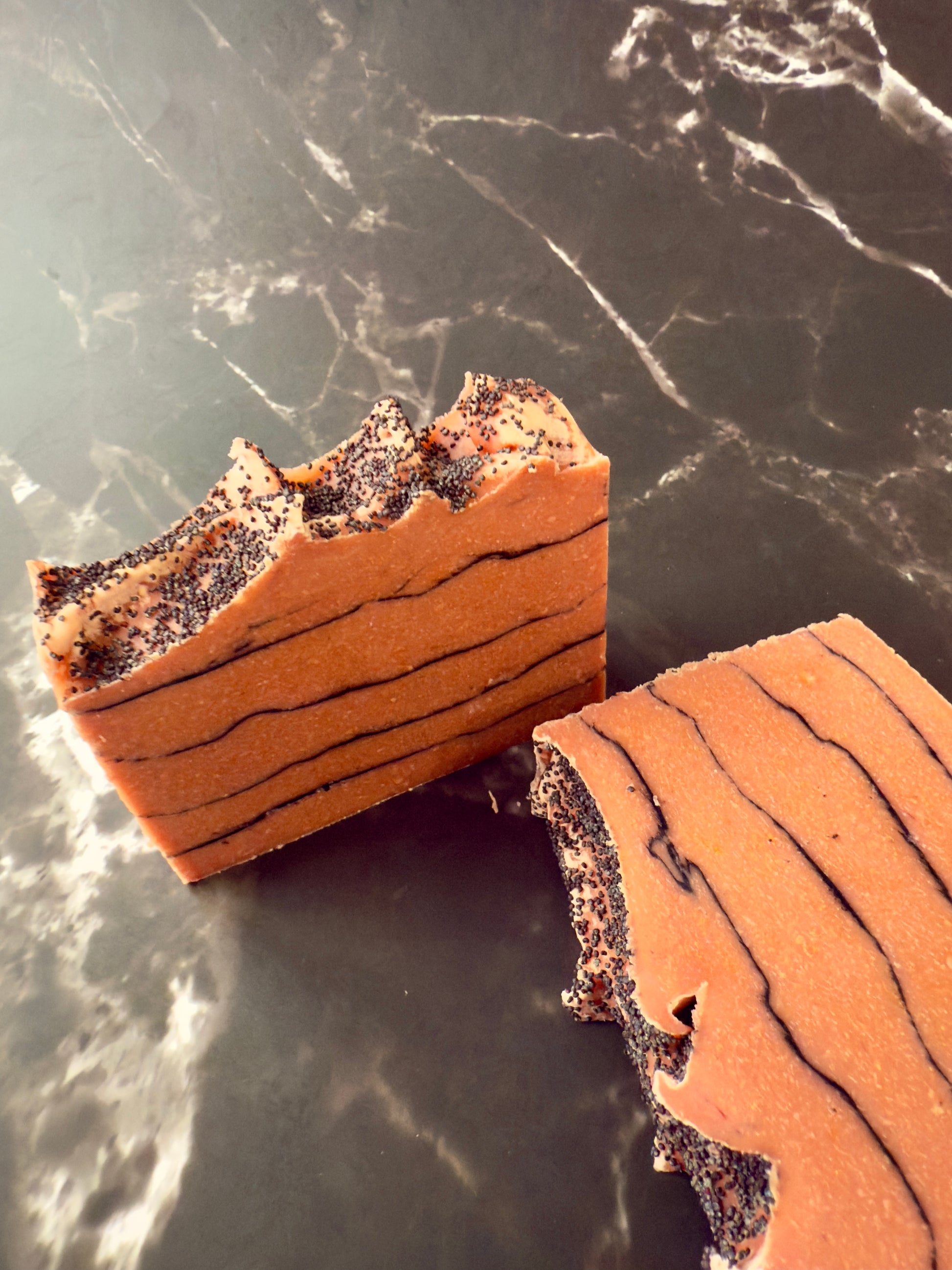 Brick-red Tomato cold process soap with black charcoal pencil lines and poppy-seed top, displayed on dark marble.