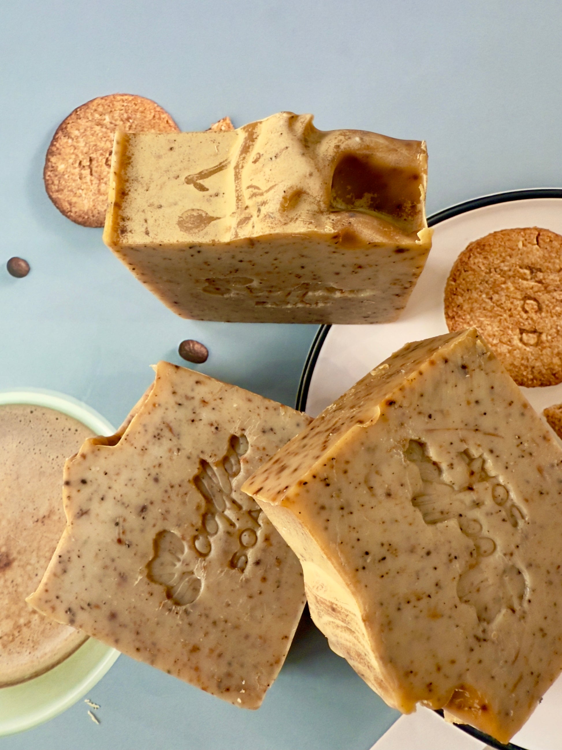 Handcrafted coffee soap bar with dry coffee specks and textured top, photographed with coffee beans and latte elements.
