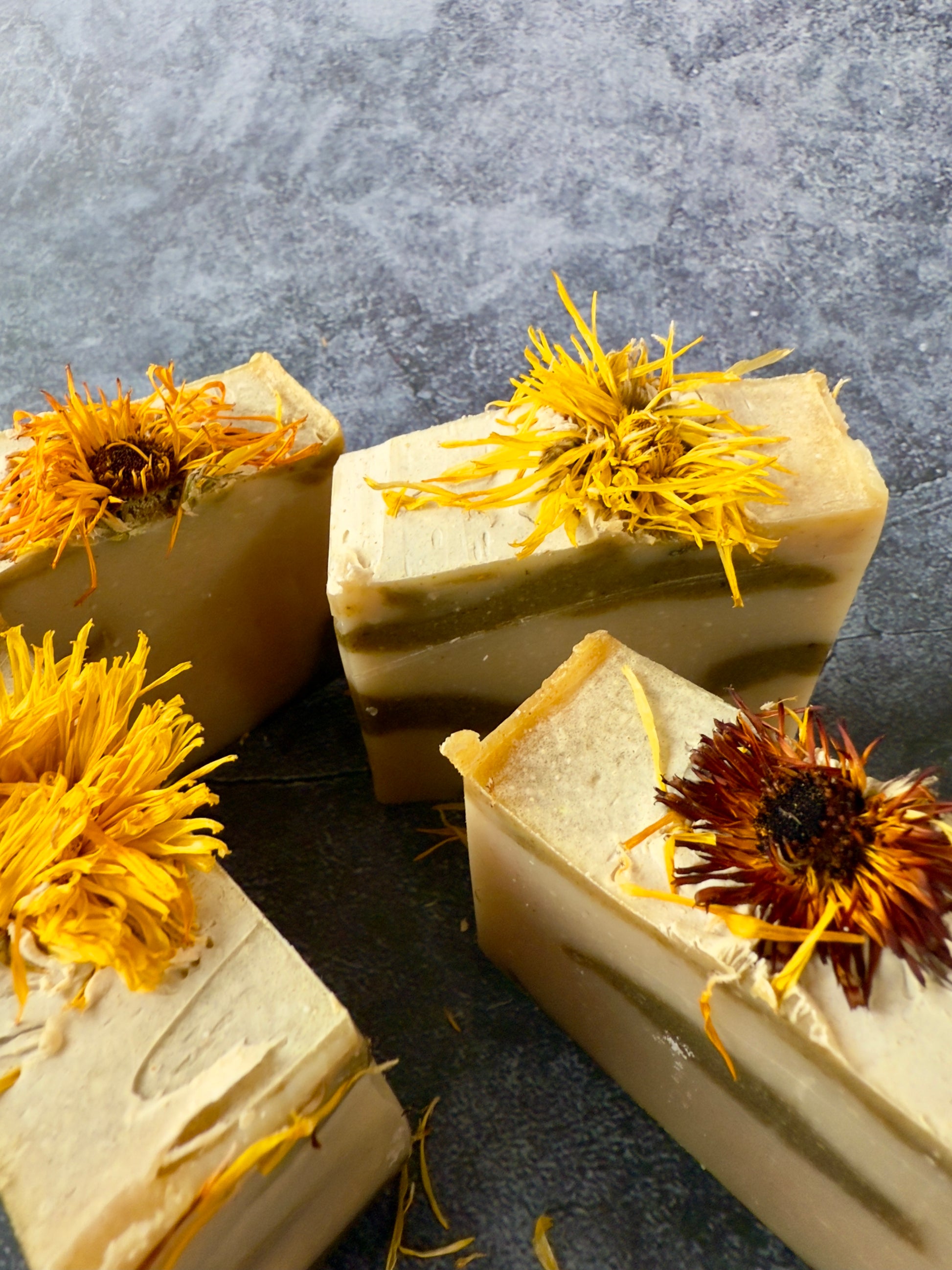 Bar soaps with yellow and brown dried flowers on a dark surface