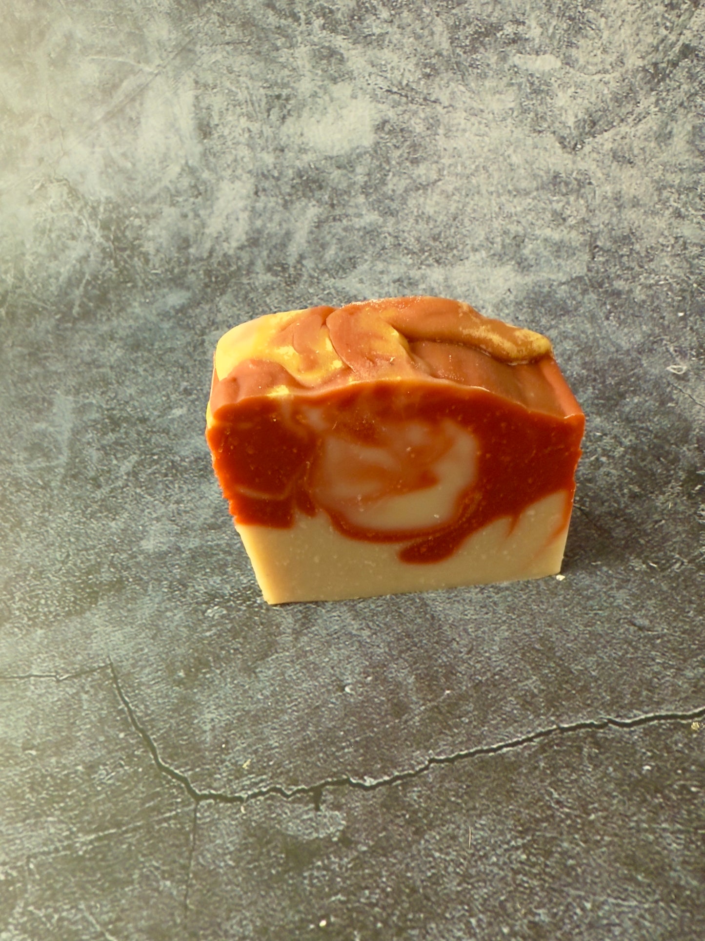 Handcrafted soap bars with warm reddish and beige clay swirls against a textured slate background.