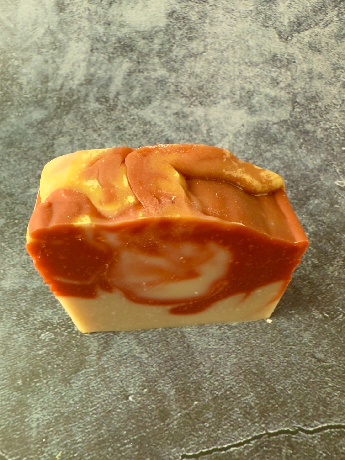 Handcrafted soap bars with warm reddish and beige clay swirls against a textured slate background.