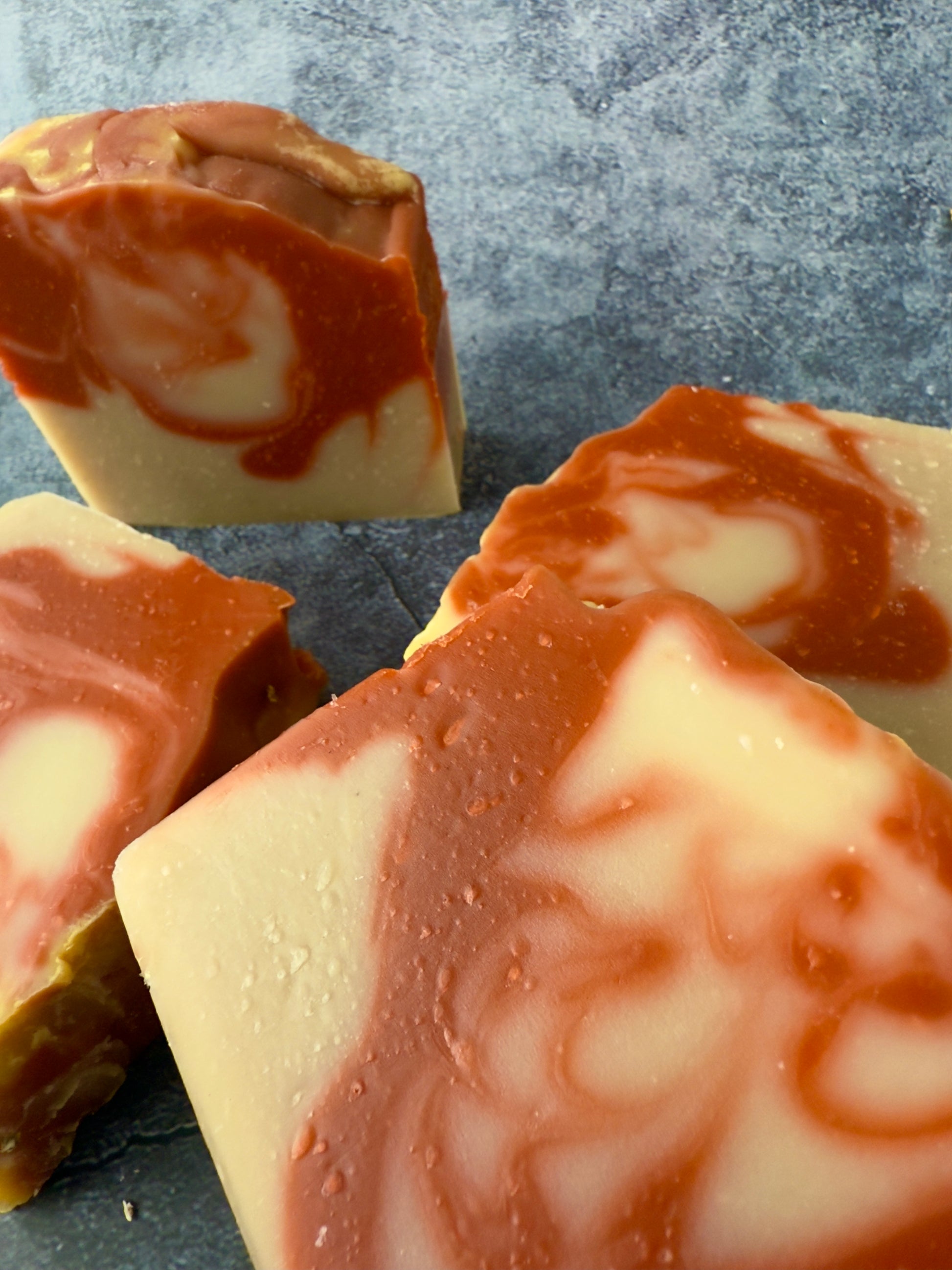 Handcrafted soap bars with warm reddish and beige clay swirls against a textured slate background.