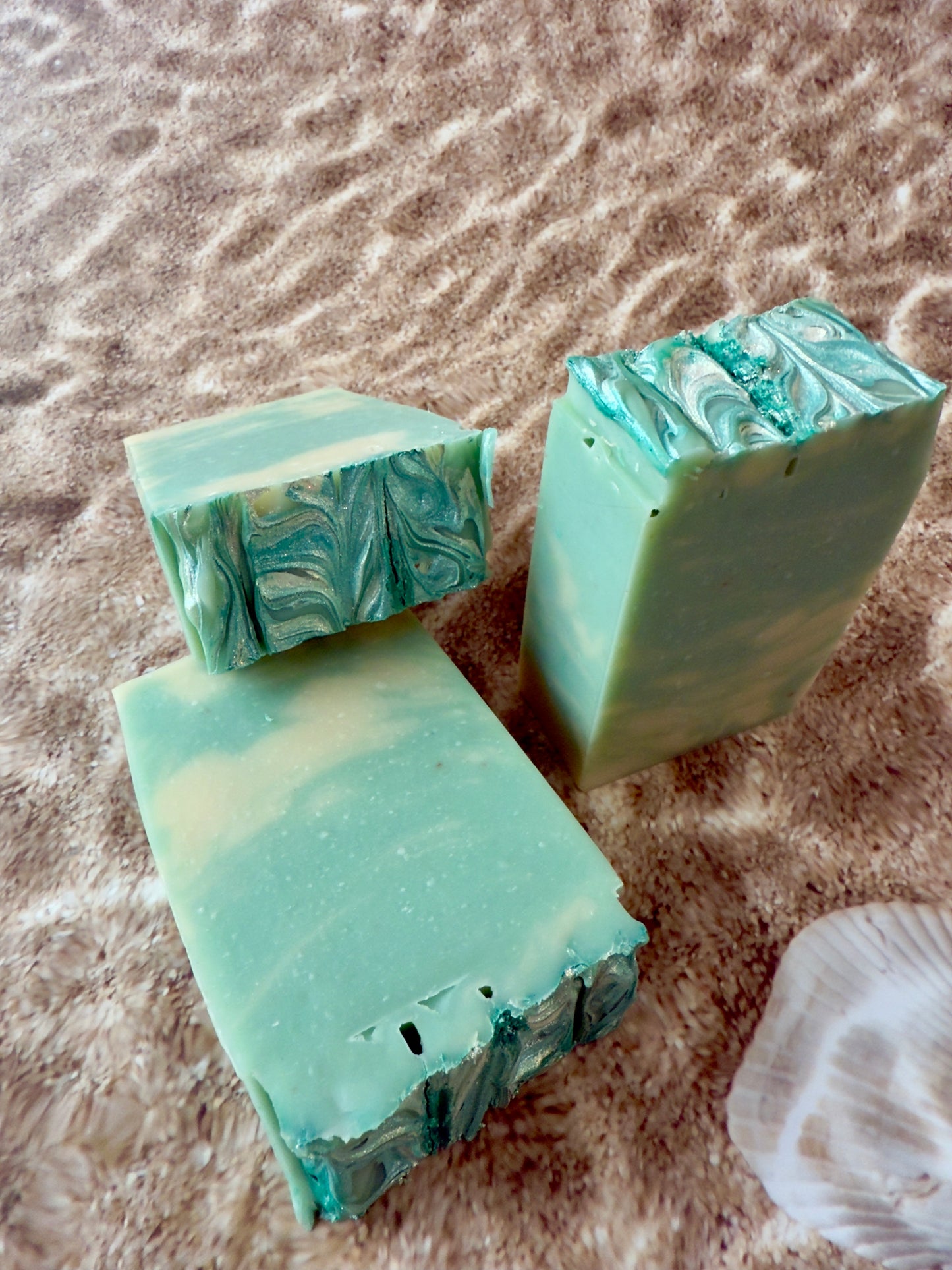 Three bars of green marbled soap on a sandy surface