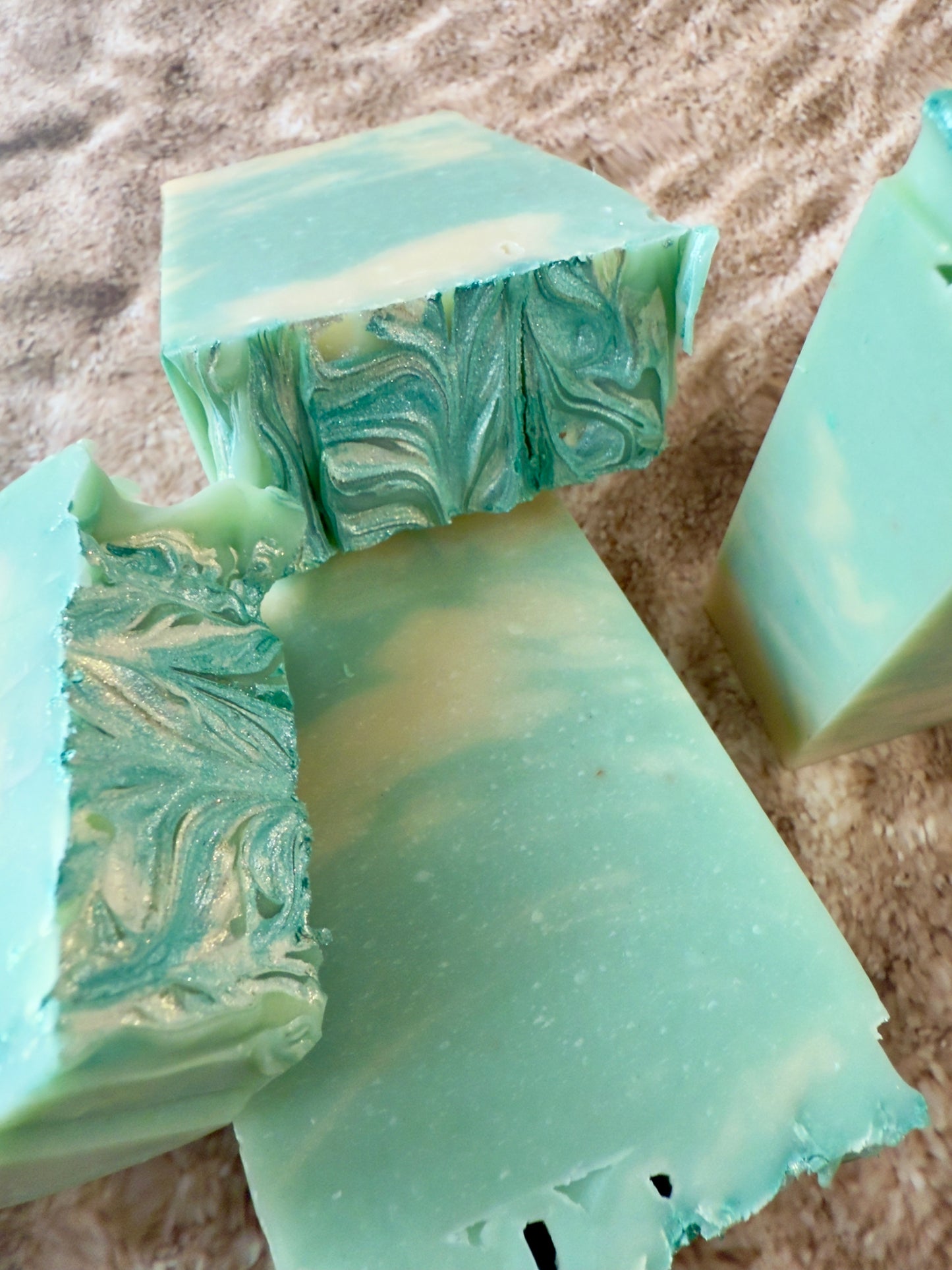 Green marbled soap bars on a textured sandy surface