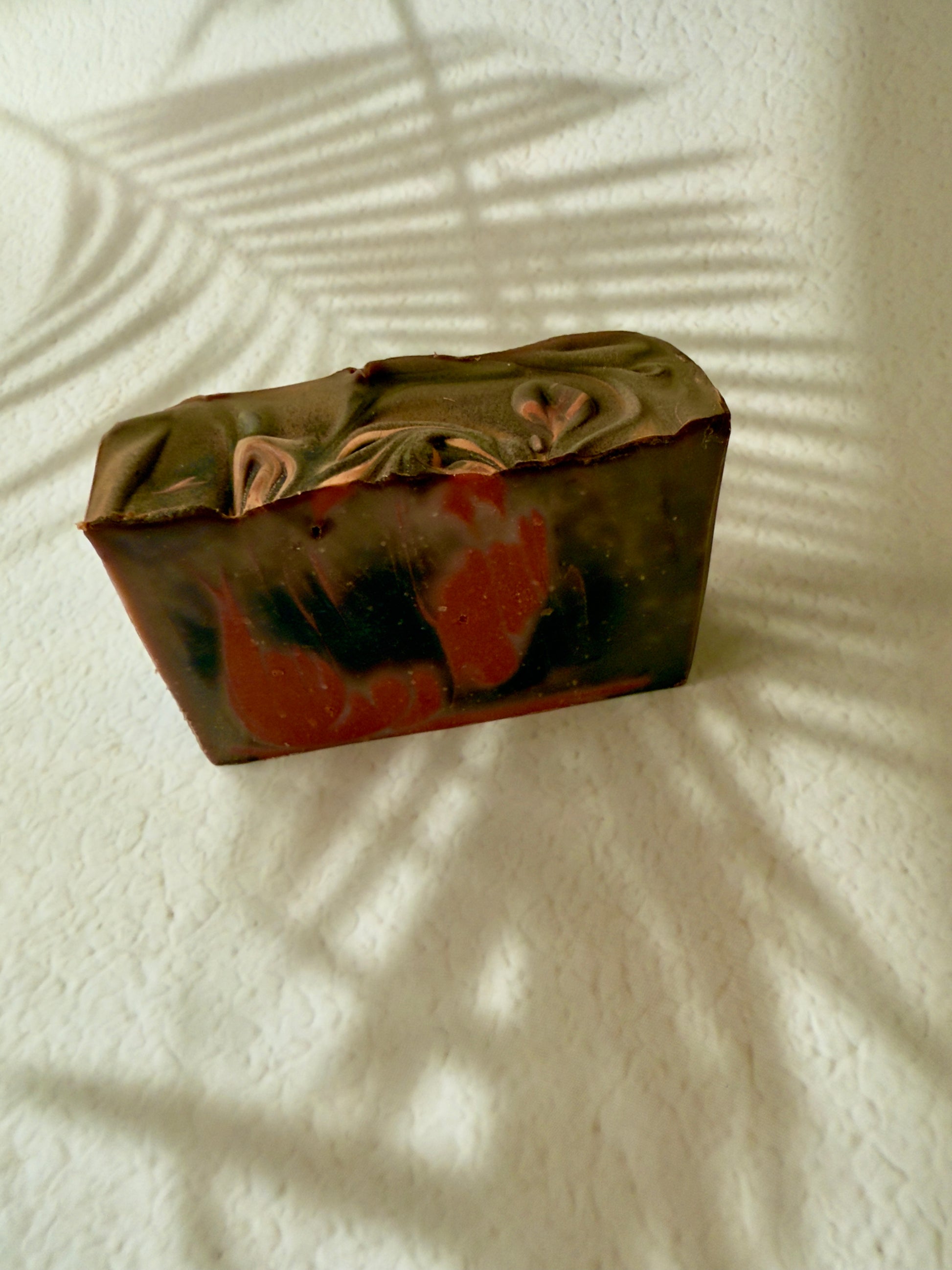 Brown and red swirled artisan soap with a creamy textured top and warm-toned marbled interior.