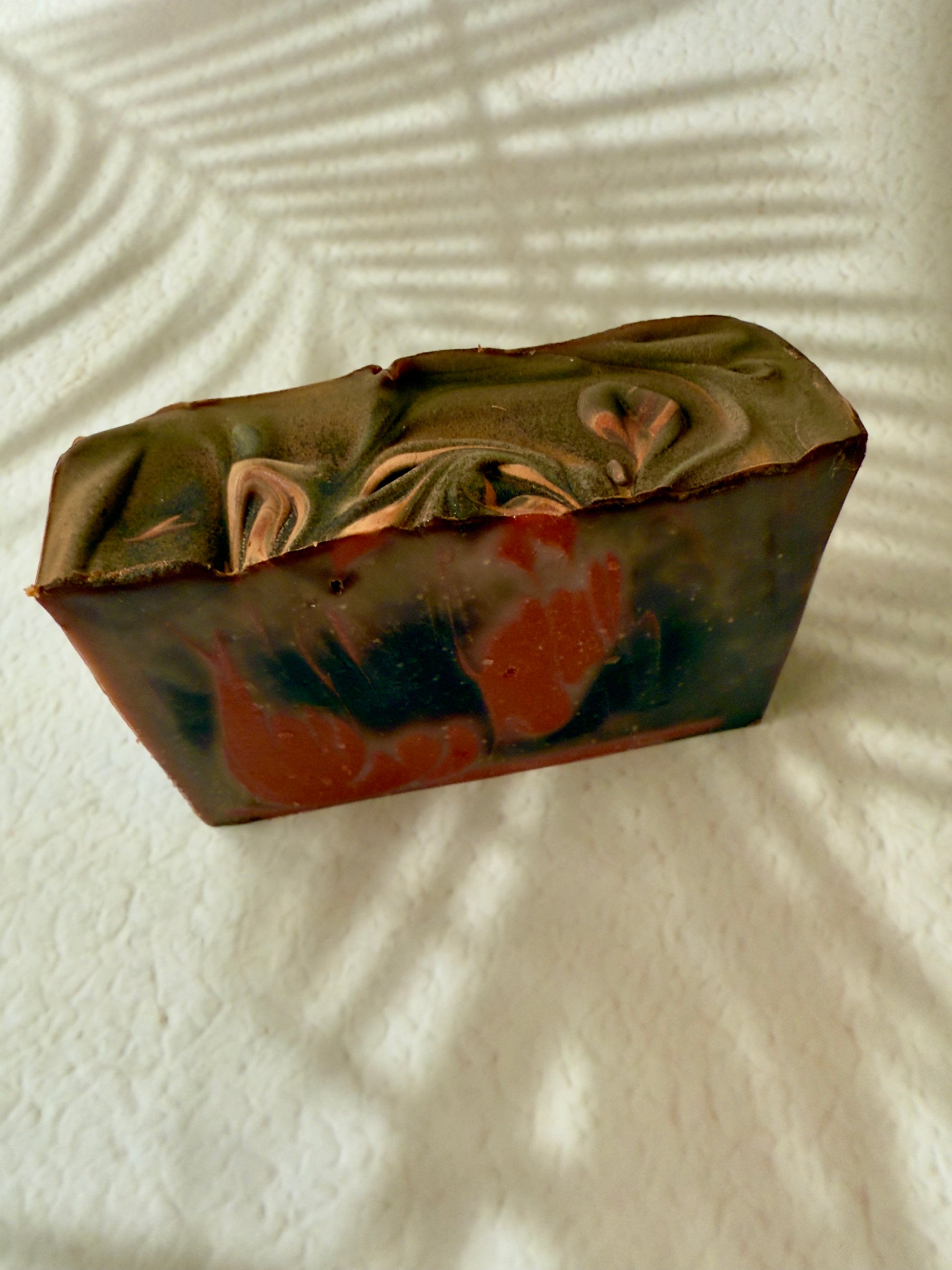 Brown and red swirled artisan soap with a creamy textured top and warm-toned marbled interior.