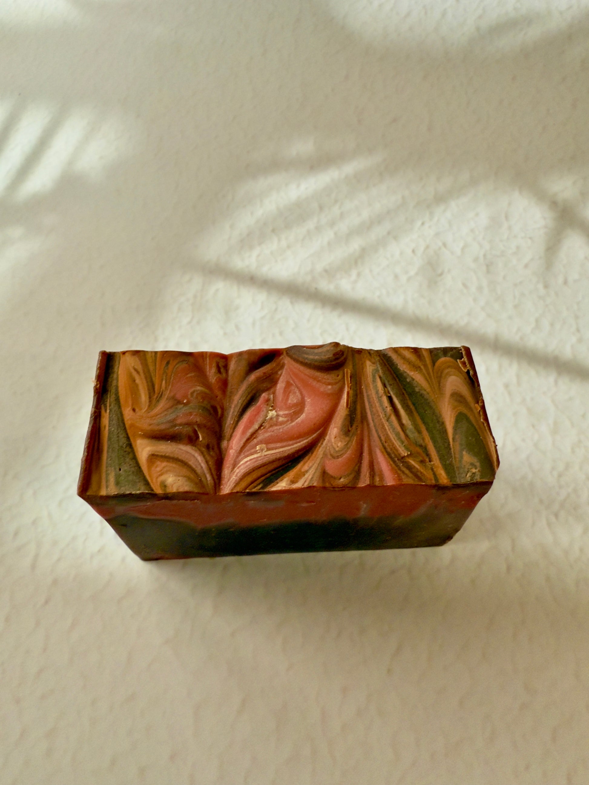 Brown and red swirled artisan soap with a creamy textured top and warm-toned marbled interior.