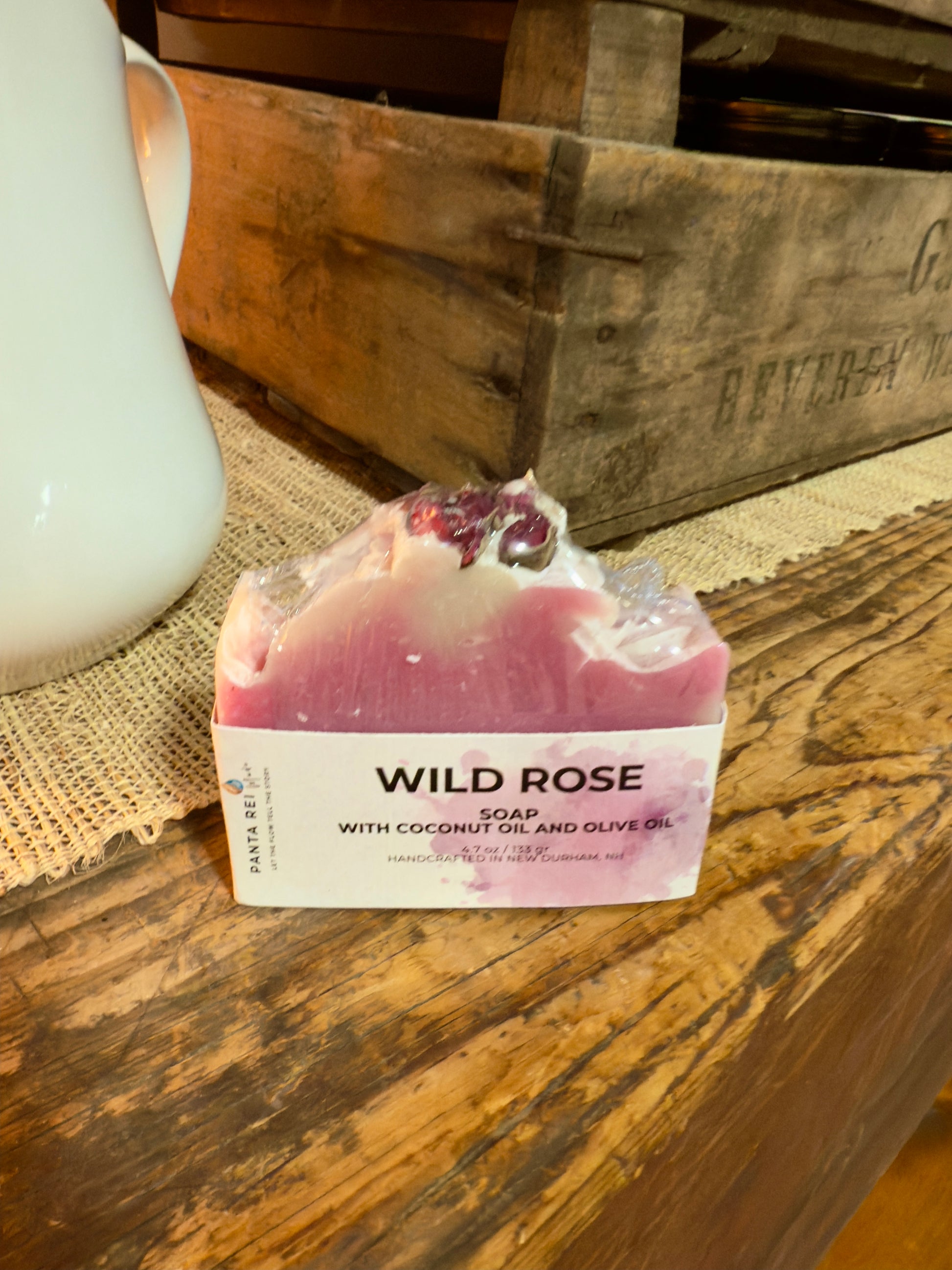 Pink two-tone rose soap bar with a textured top and dried rose buds, displayed on a rustic wooden surface.