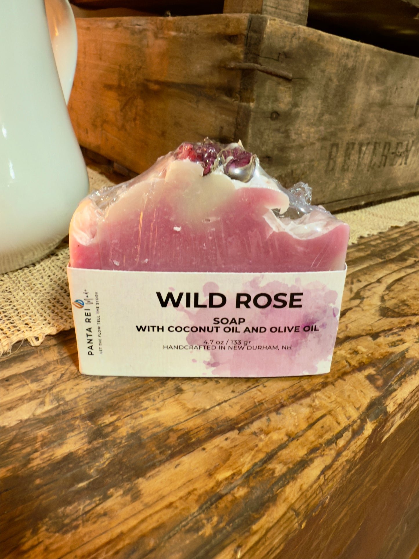 Pink two-tone rose soap bar with a textured top and dried rose buds, displayed on a rustic wooden surface.