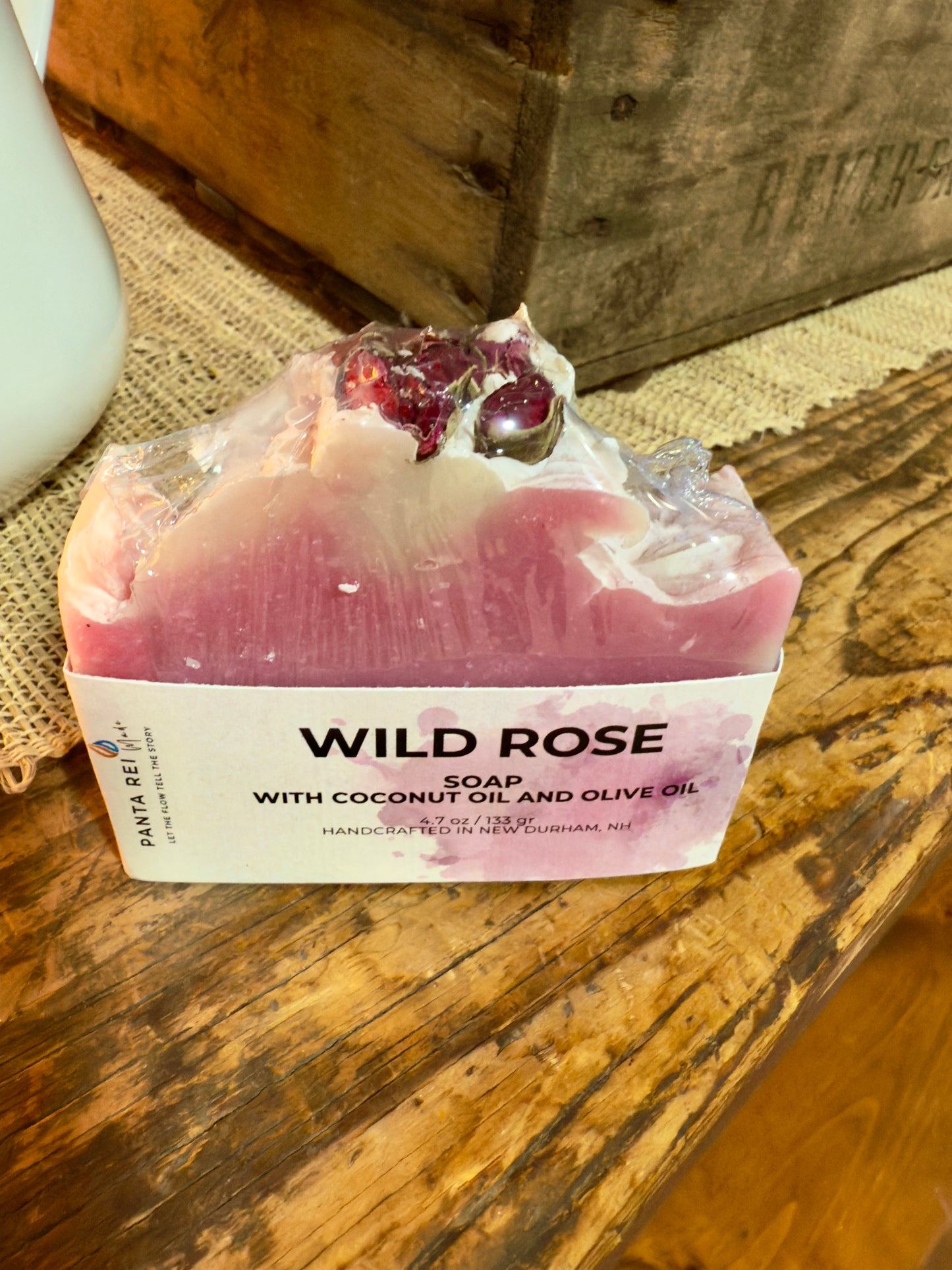 Pink two-tone rose soap bar with a textured top and dried rose buds, displayed on a rustic wooden surface.