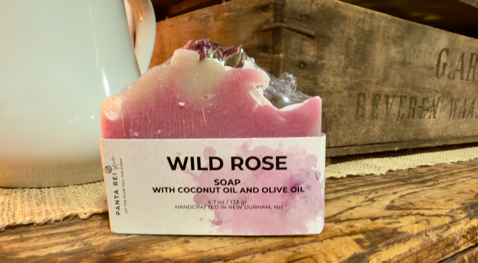 Pink two-tone rose soap bar with a textured top and dried rose buds, displayed on a rustic wooden surface.