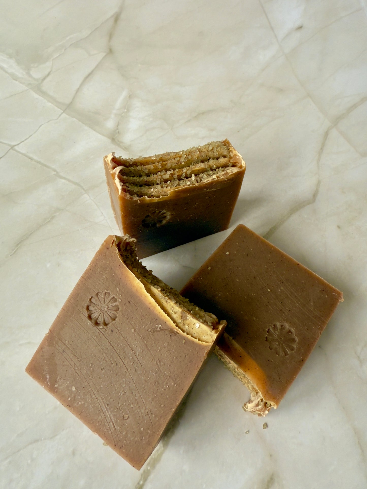 Brown artisan fig and amber soap bars with coarse salt on a marble background.