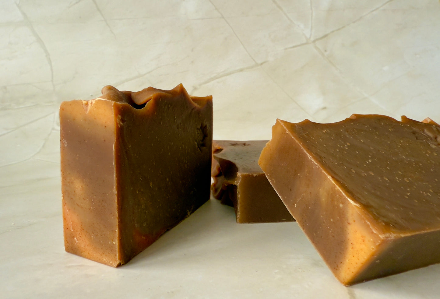 Brown artisan soap bars and round pudding-style bar with natural speckling on a marble background.