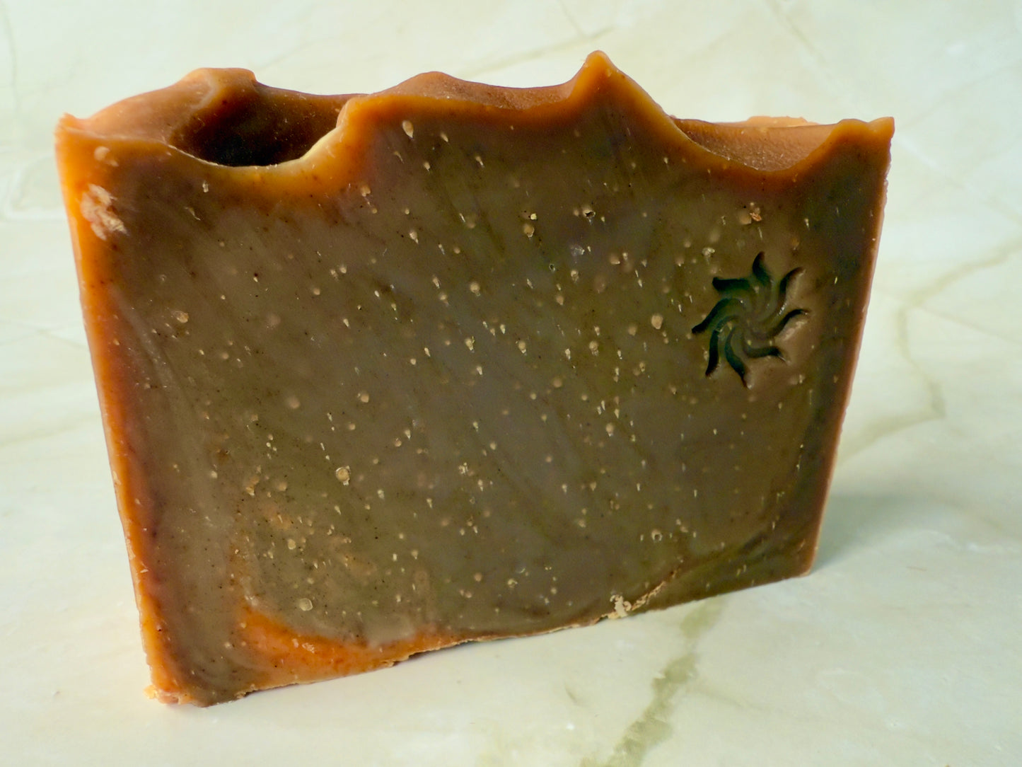Brown artisan soap bars and round pudding-style bar with natural speckling on a marble background.