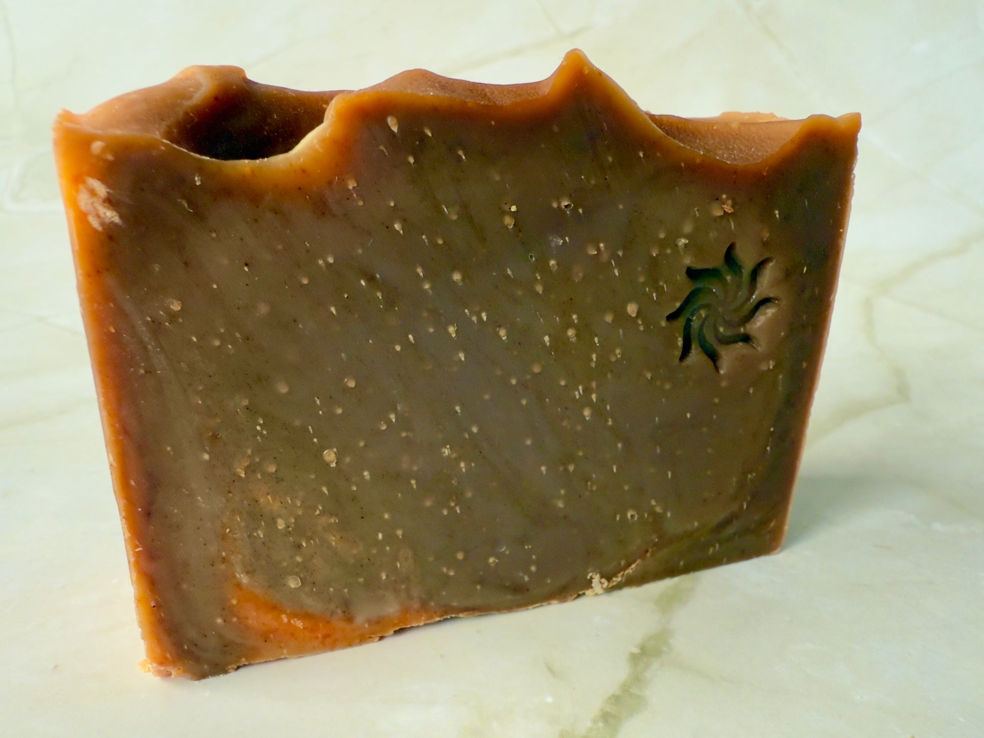 Brown artisan soap bars and round pudding-style bar with natural speckling on a marble background.