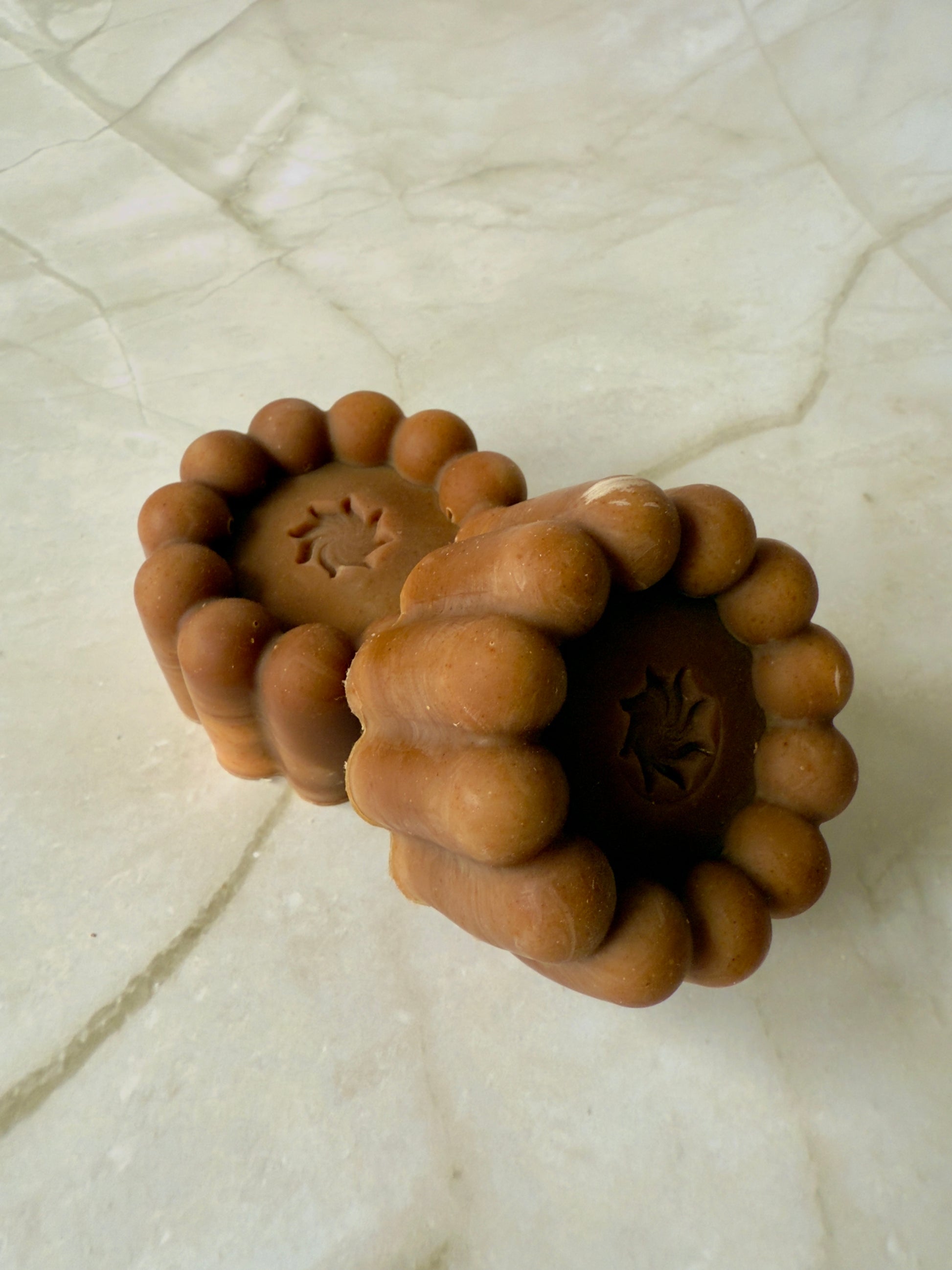 Brown artisan soap bars and round pudding-style bar with natural speckling on a marble background.
