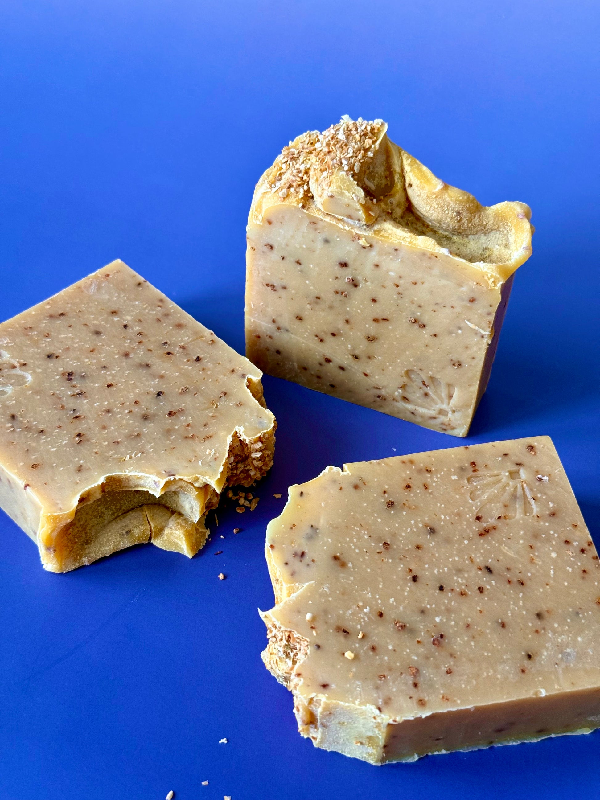 Golden citrus soap bars with orange peel speckles and a textured peel topping on a deep blue background.
