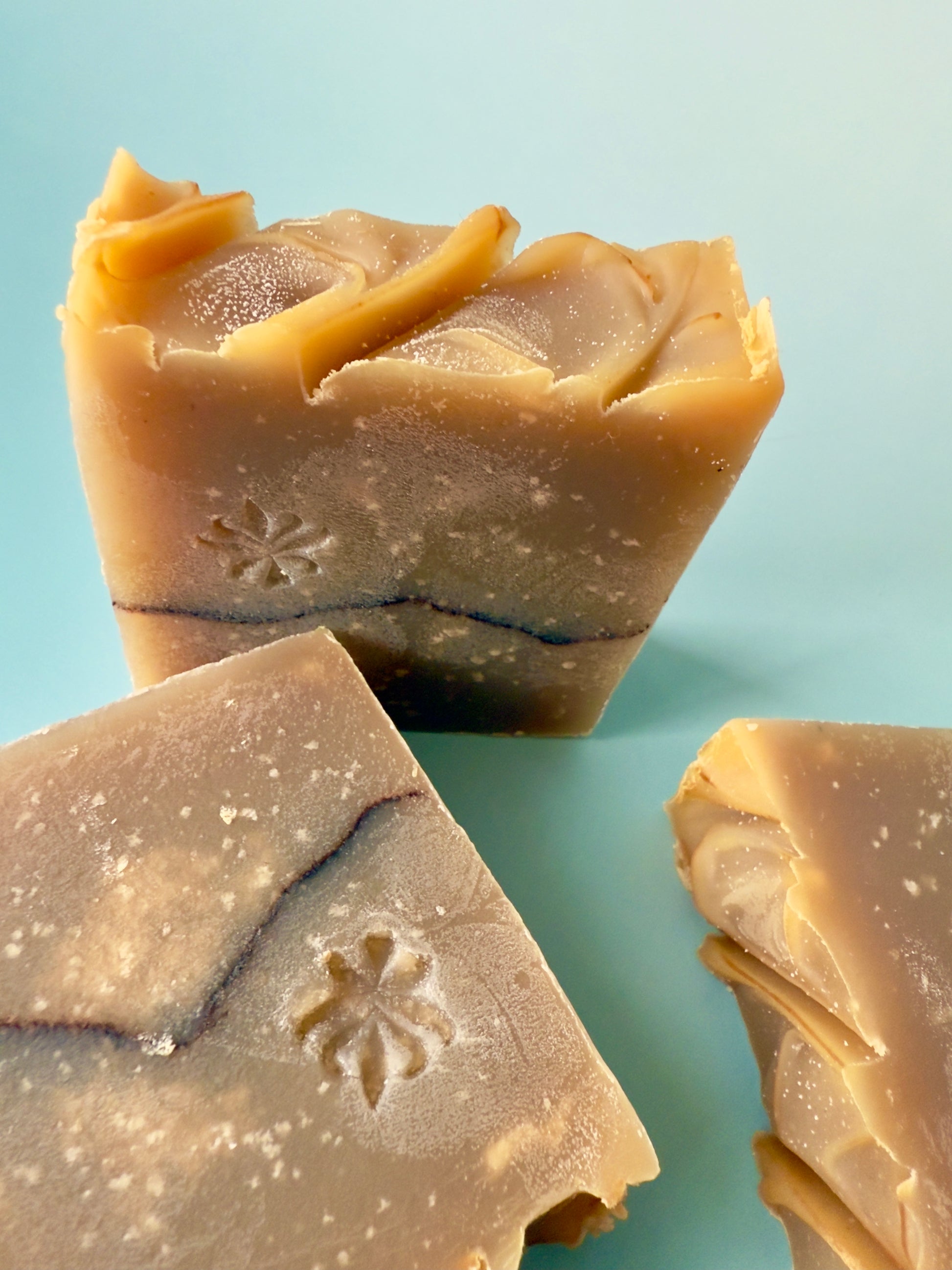 Warm tan artisan soap bars with a cocoa powder pencil line on a soft aqua background.