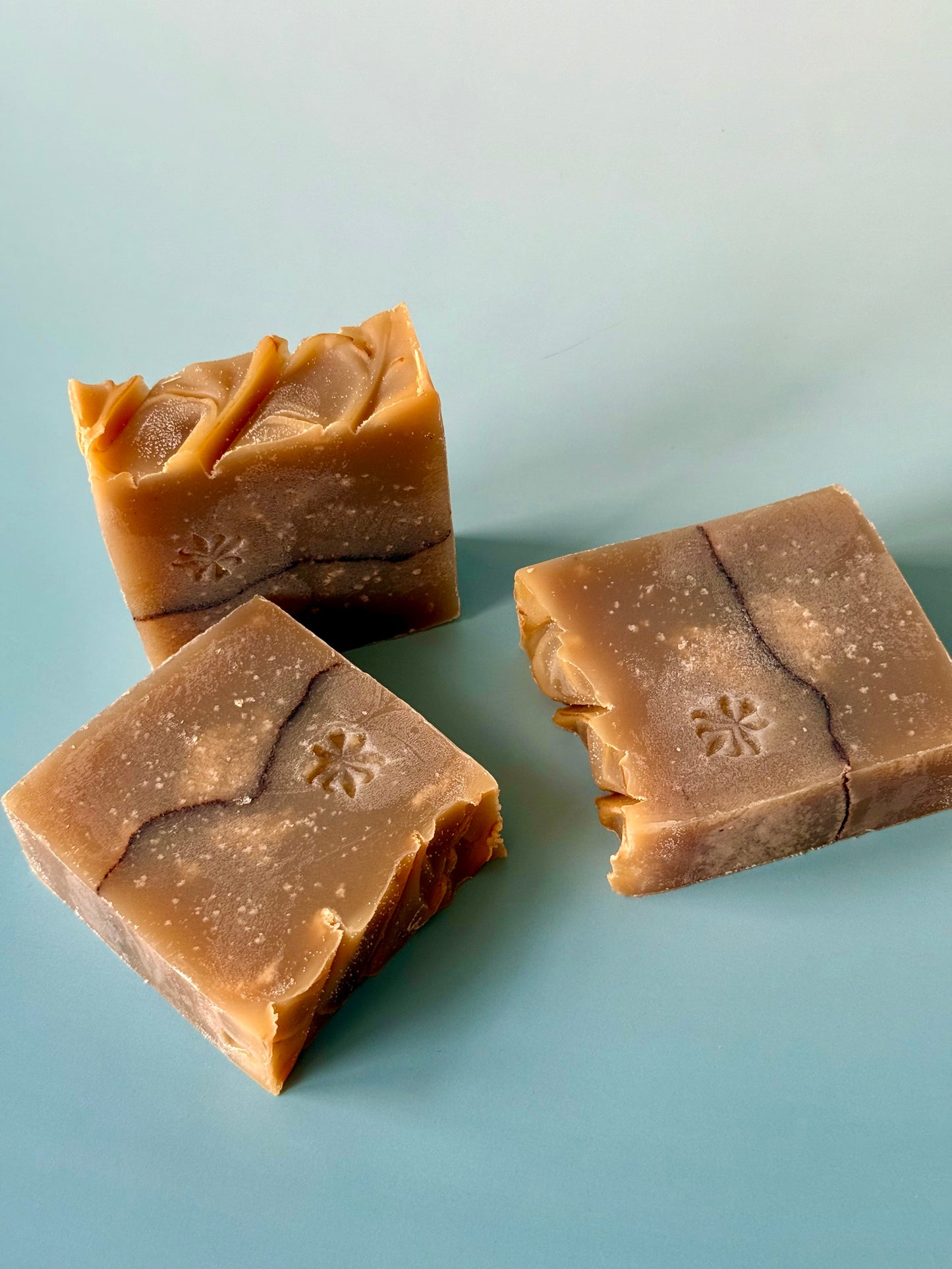 Warm tan artisan soap bars with a cocoa powder pencil line on a soft aqua background.