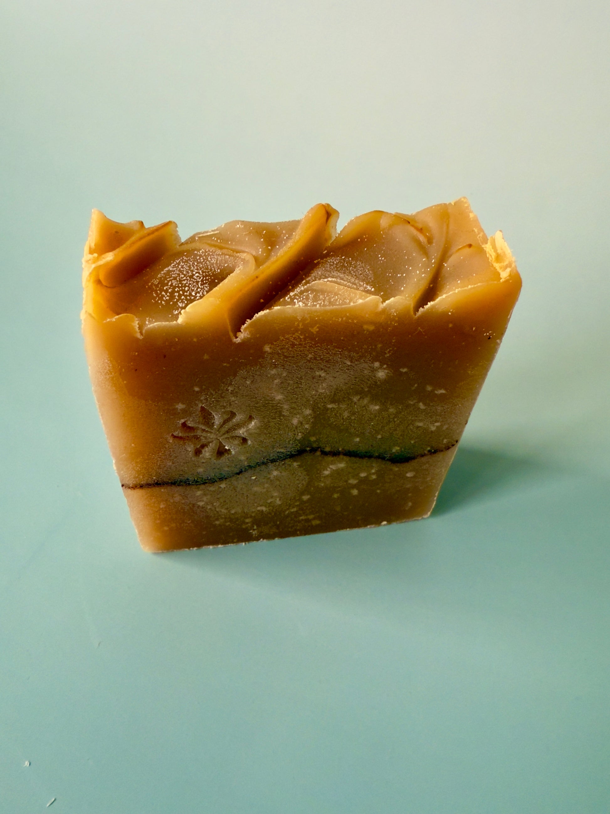 Warm tan artisan soap bars with a cocoa powder pencil line on a soft aqua background.