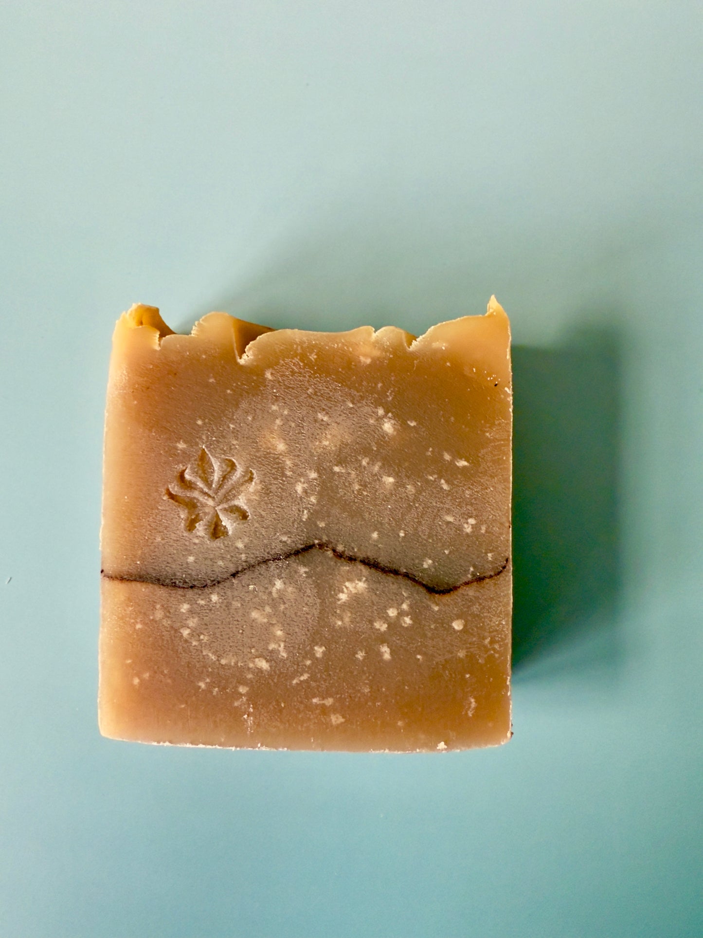 Warm tan artisan soap bars with a cocoa powder pencil line on a soft aqua background.