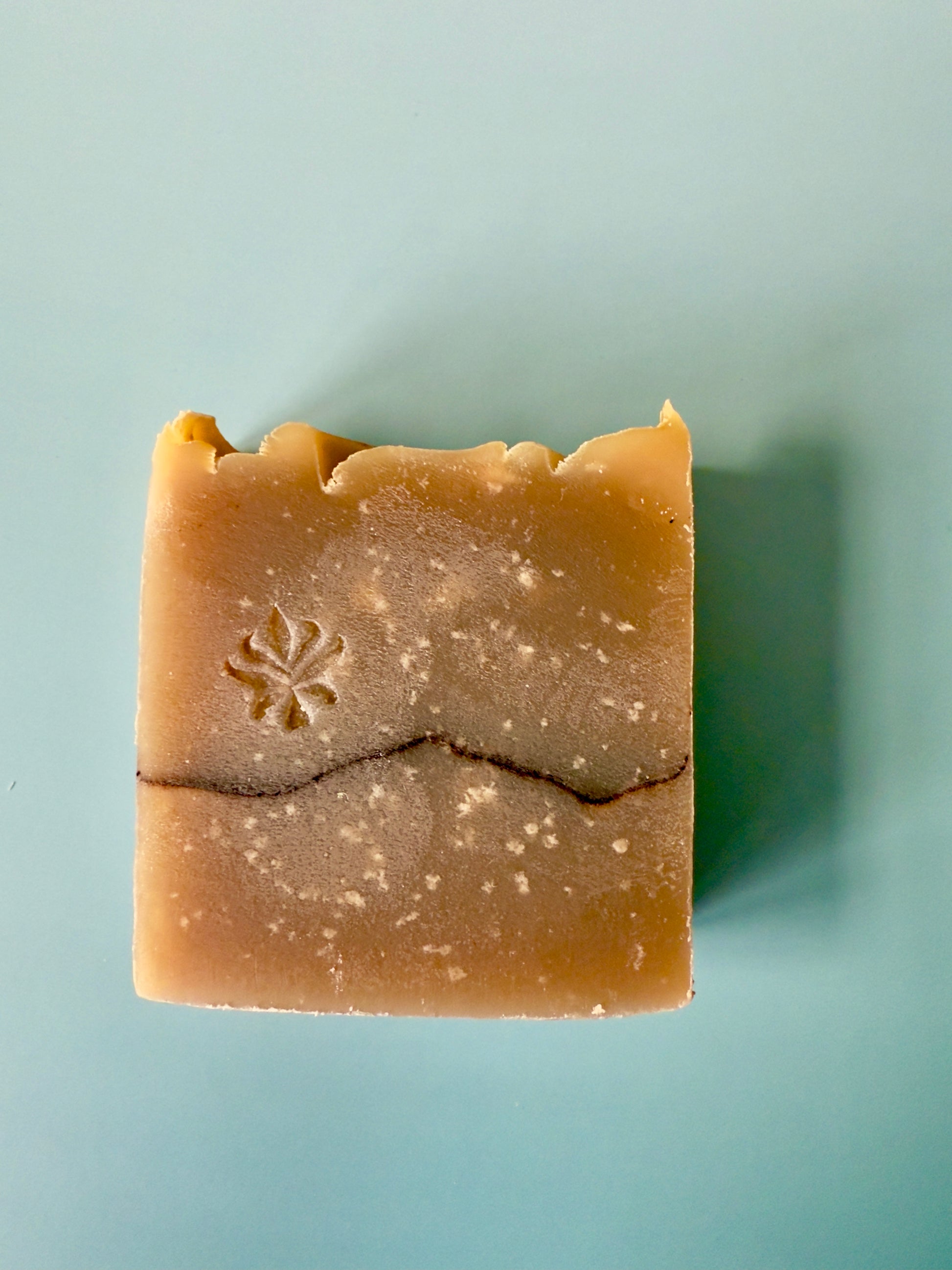 Warm tan artisan soap bars with a cocoa powder pencil line on a soft aqua background.