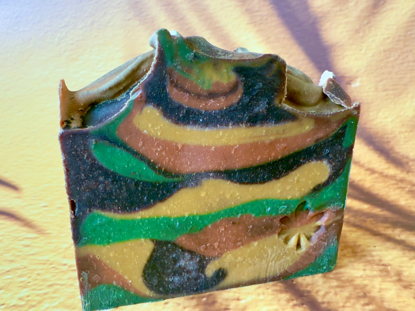 Artisan soap bar with green, gold, brown, and amber swirls on a warm desert-toned background.