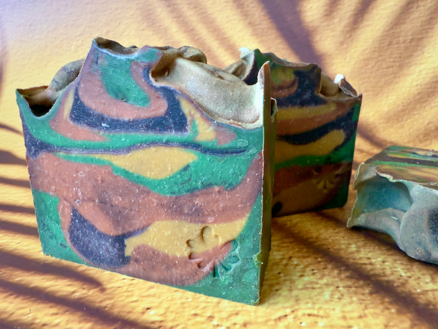 Artisan soap bar with green, gold, brown, and amber swirls on a warm desert-toned background.