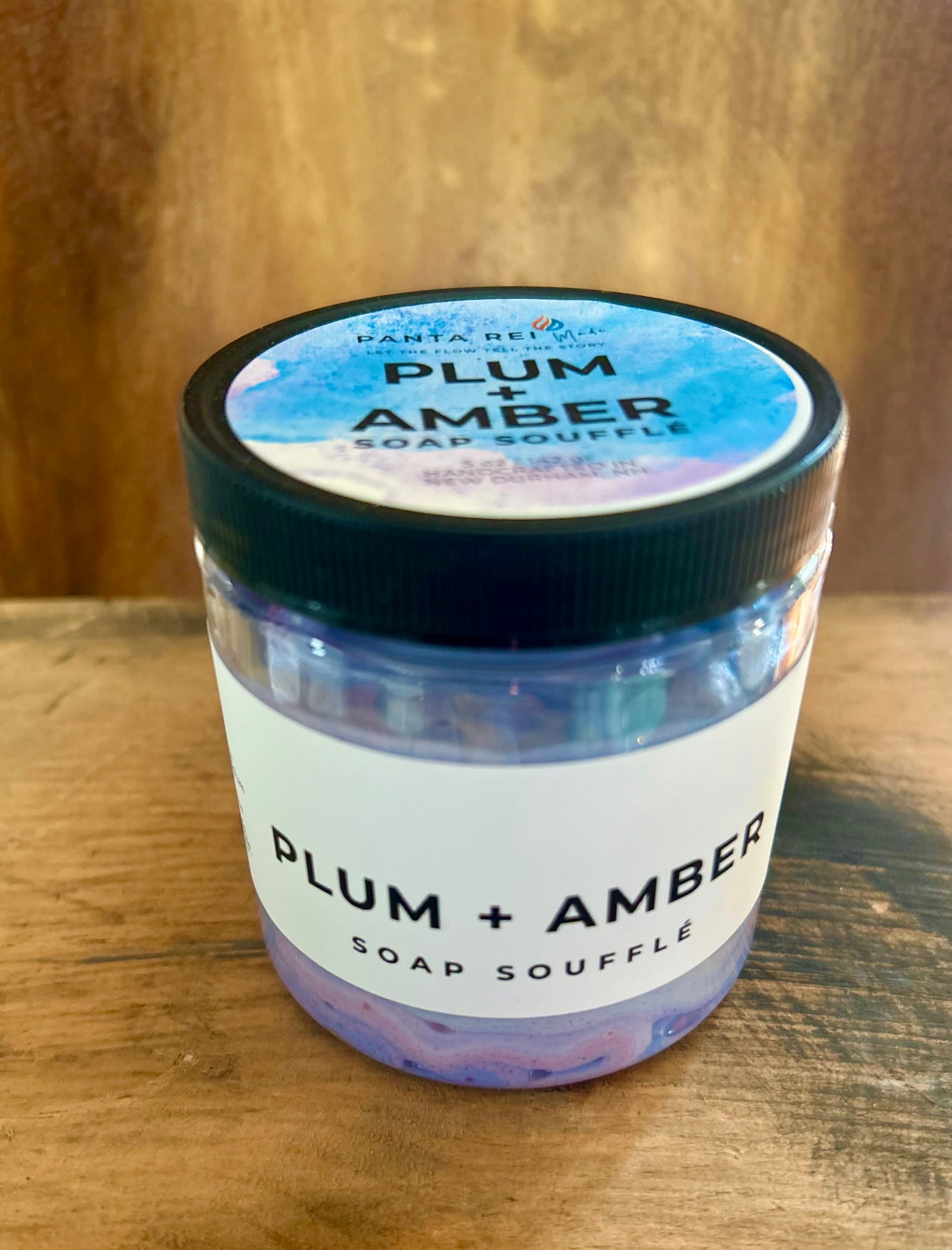 “Plum + Amber Soap Soufflé in a clear jar with purple and peach whipped swirls.”