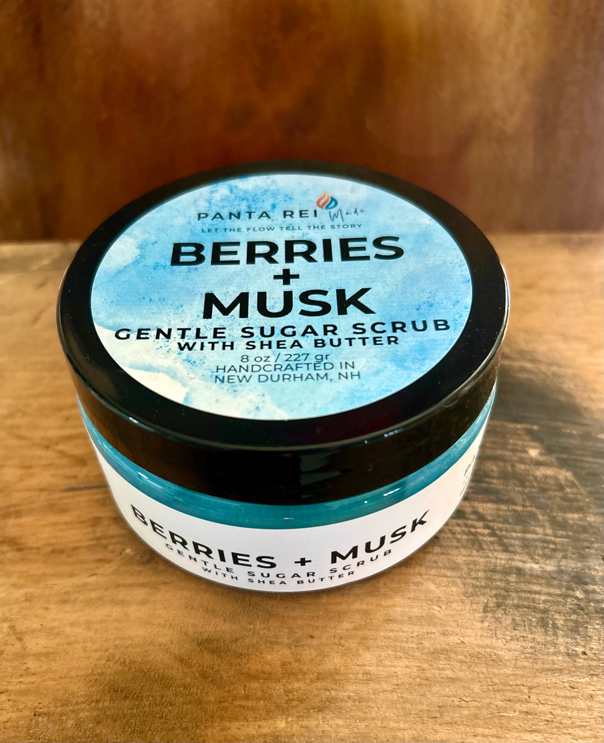 Blue Berries + Musk gentle sugar scrub in clear jar with black lid on wood surface.