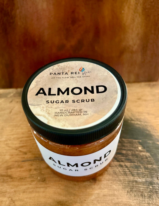 Almond sugar scrub jar on wood surface with black lid and tan label.
