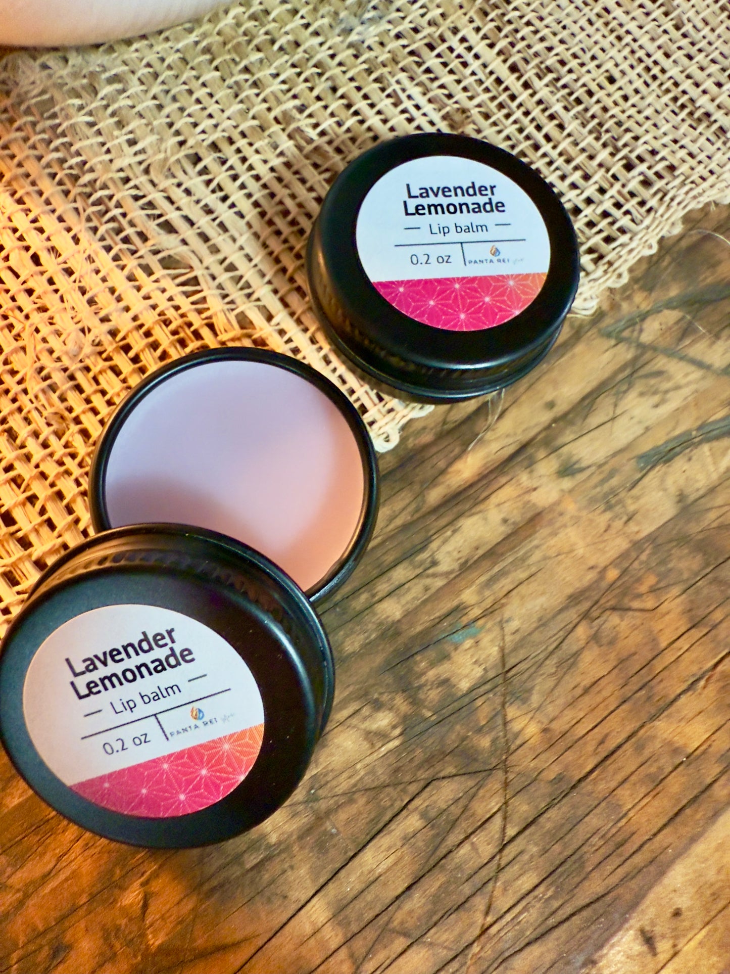 Lavender Lemonade lip balm in a black tin on a wooden surface. Open tin of Lavender Lemonade lip balm showing smooth balm surface.