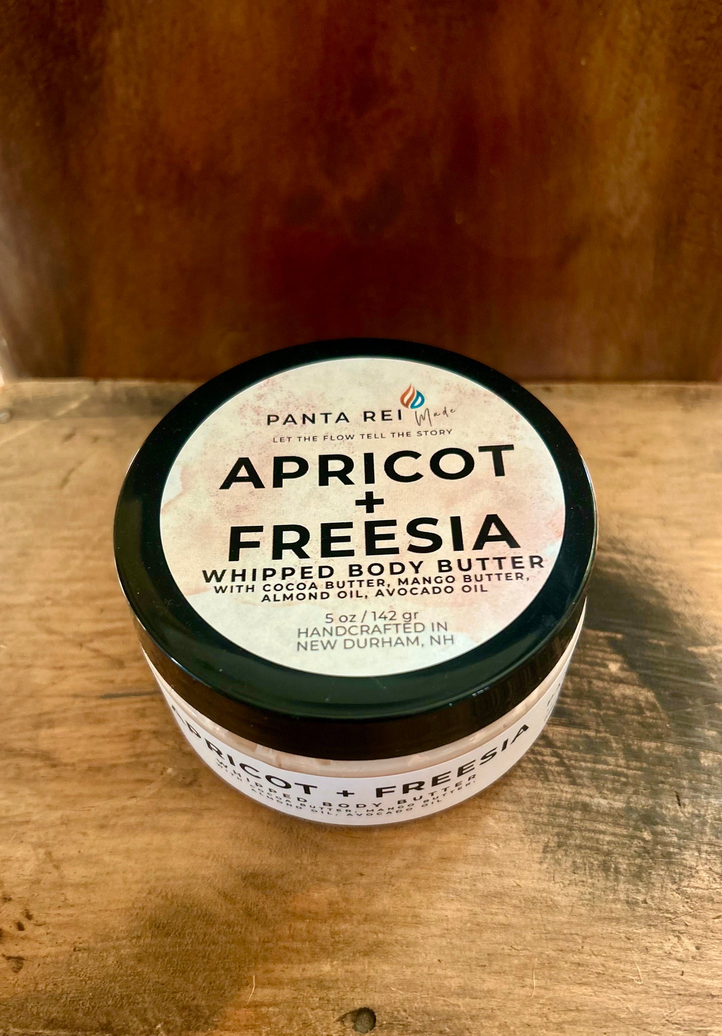 “Apricot + Freesia Whipped Body Butter in a clear jar with a warm sunset-orange tone.”