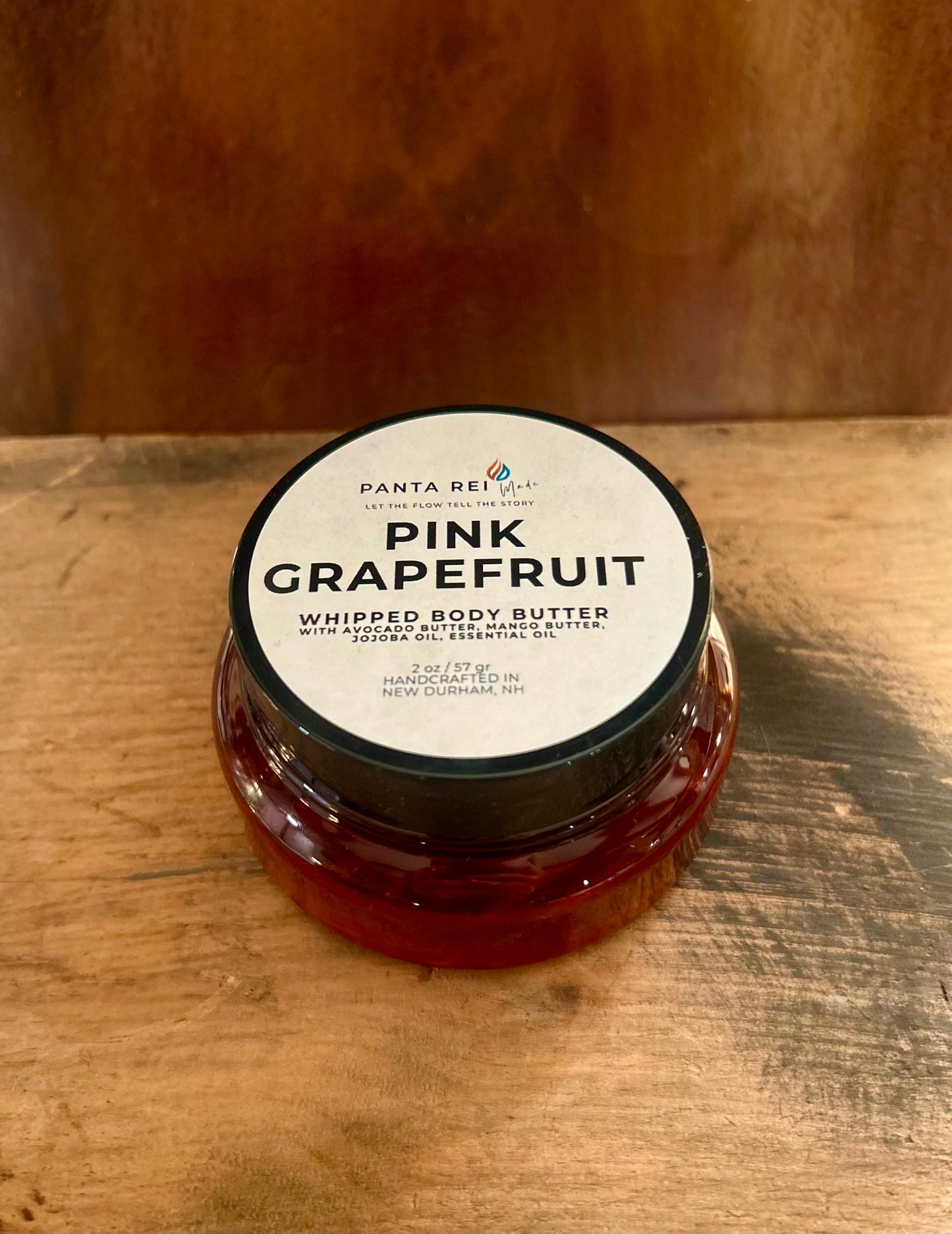 Small amber jar of Pink Grapefruit Whipped Body Butter displayed on a wooden surface, showing a lightweight citrus-infused body butter.