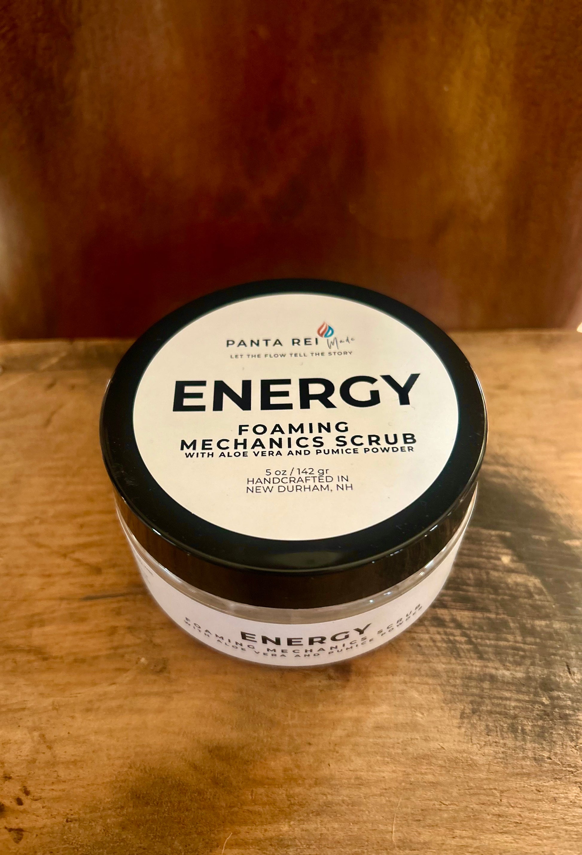 Energy foaming mechanic scrub in a black-lid jar with a minimalist label, photographed on a warm wood surface.