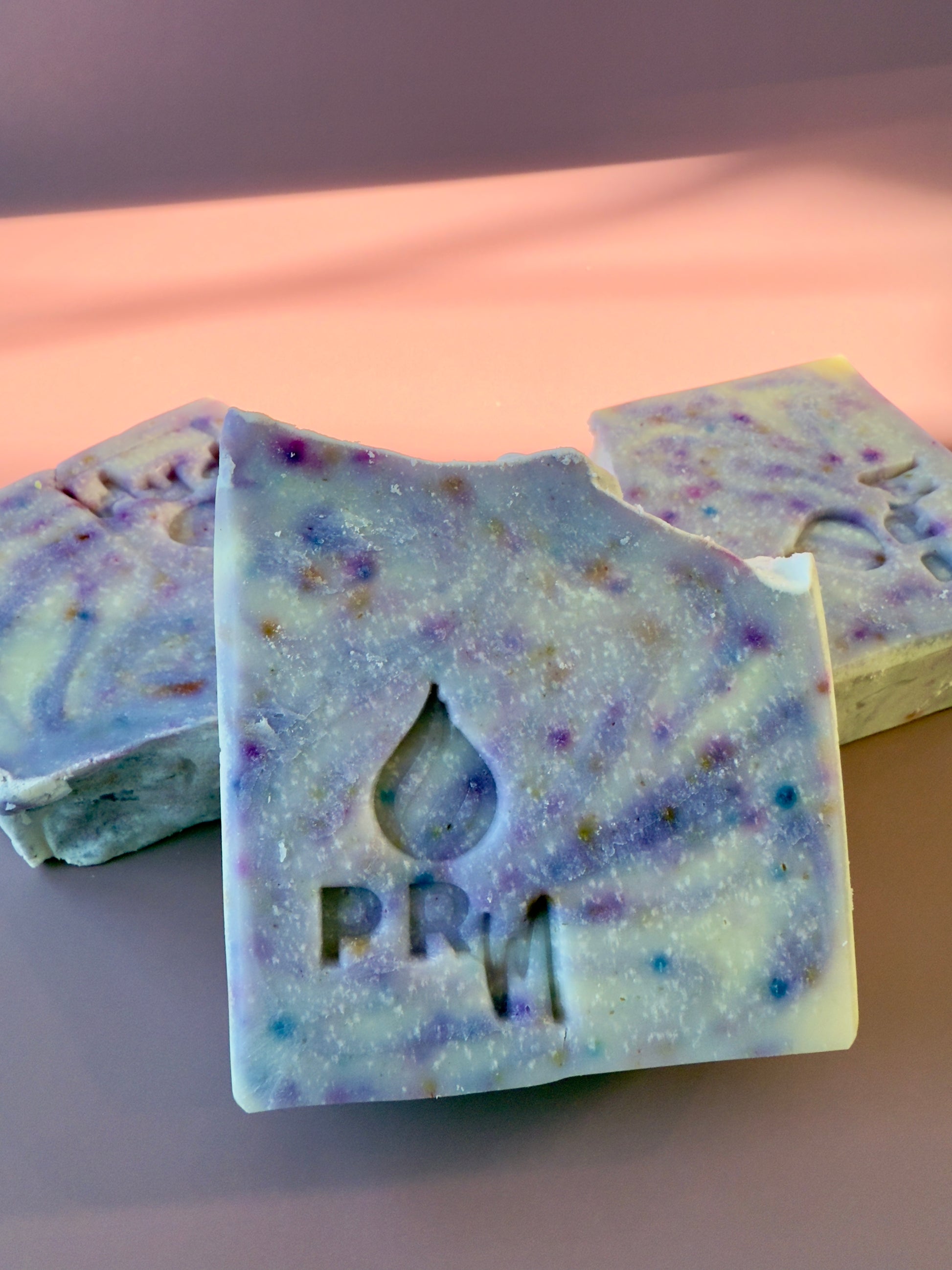 Three bars of soap with a marbled design on a pink background