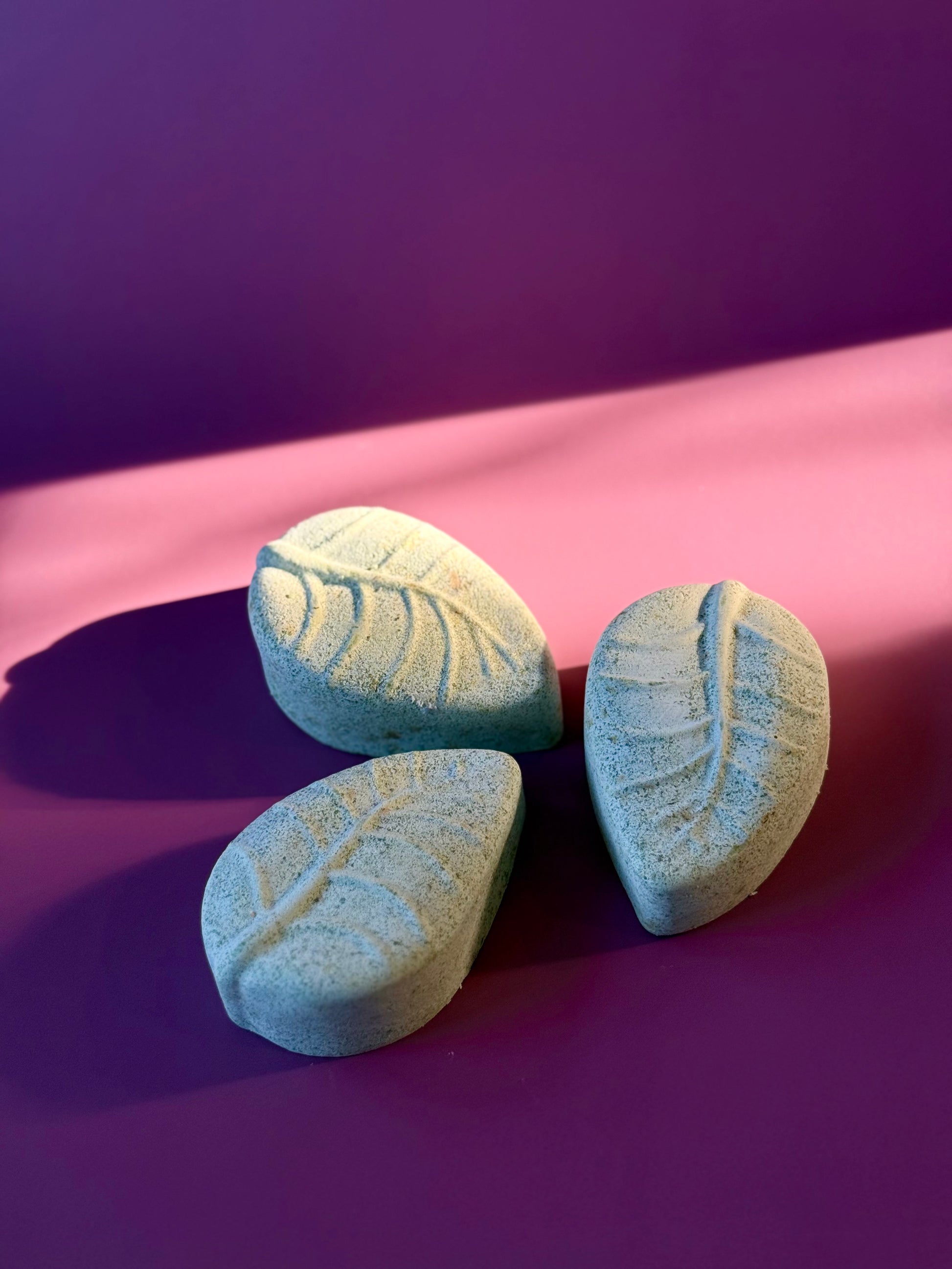 Three green leaf-shaped soap bars on a purple background