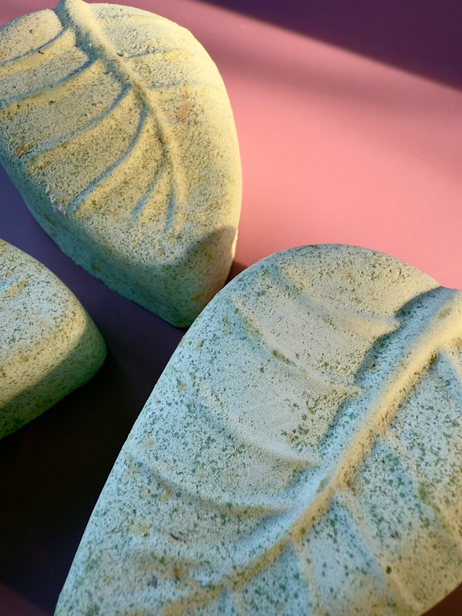 Two leaf-shaped soap bars with textured surfaces on a pink and purple gradient background