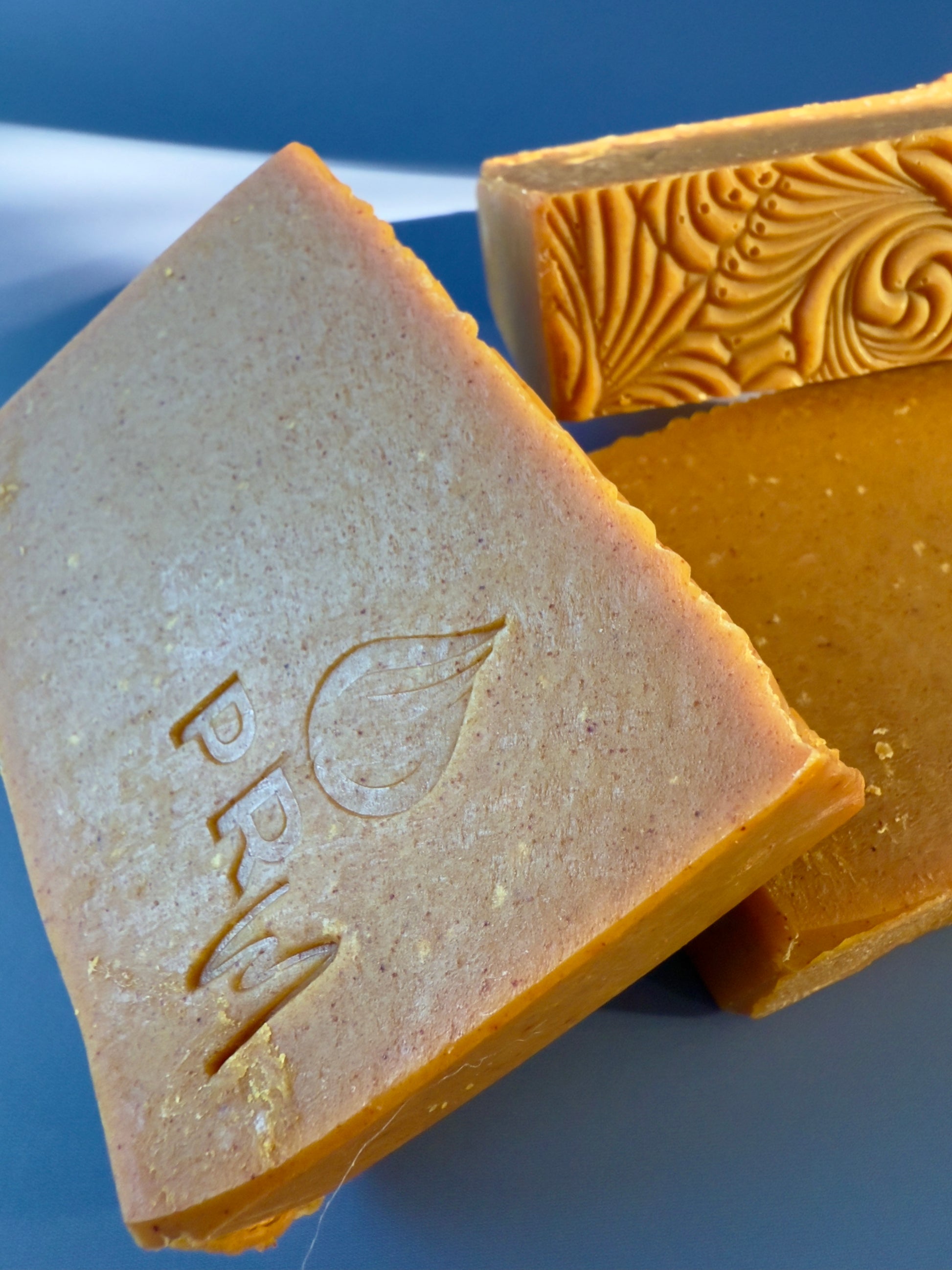 Three bars of orange-colored soap with a brand logo on a blue background