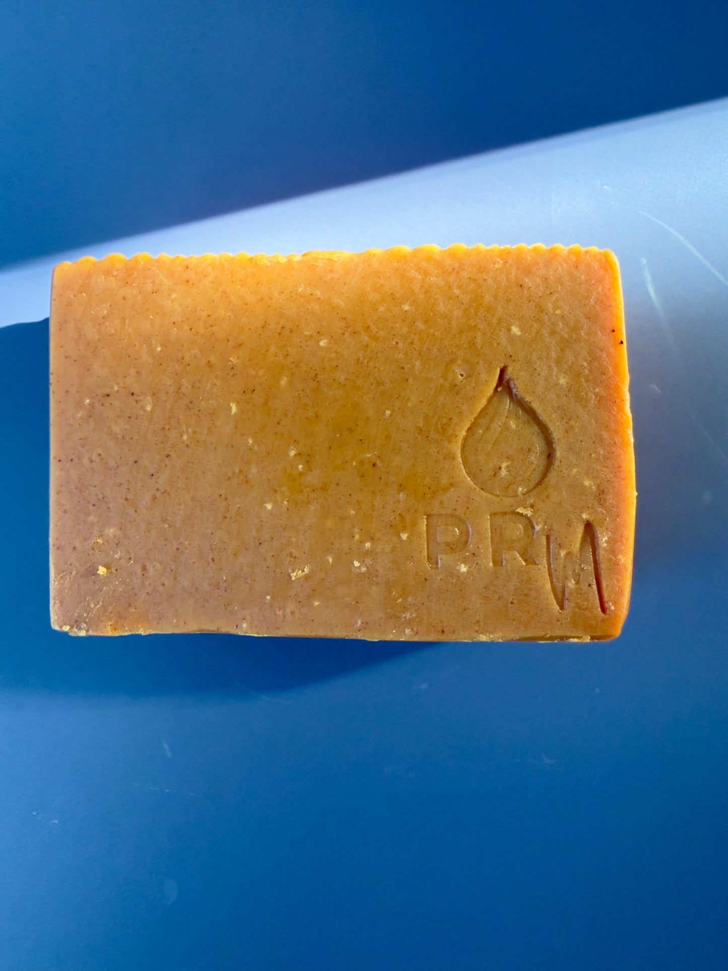 Bar of soap with natural turmeric color,  a PRM logo on a blue background