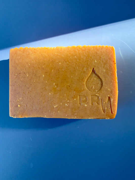 Bar of soap with natural turmeric color,  a PRM logo on a blue background
