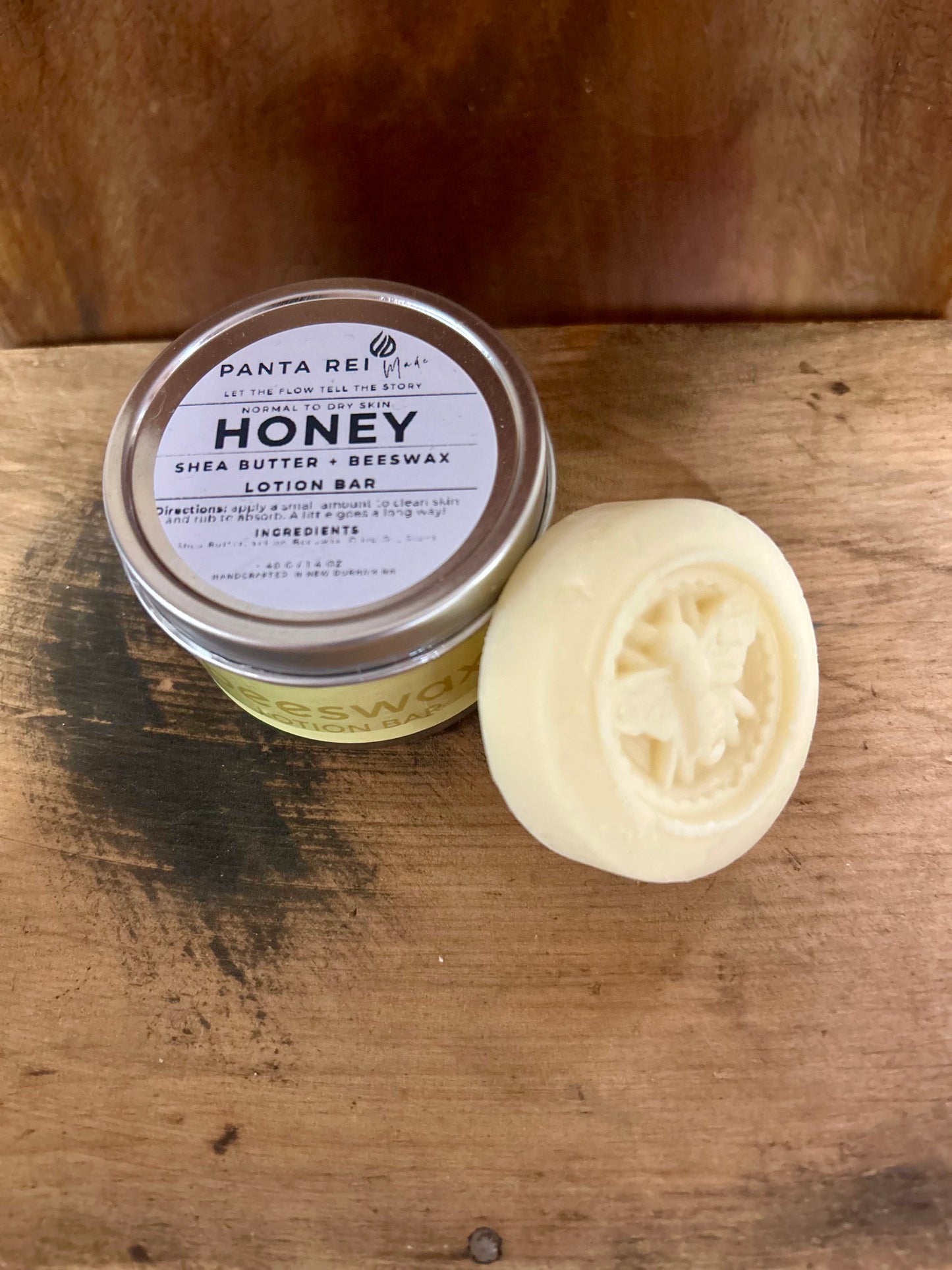Honey lotion bar in a tin with a carved honeybee design, shown on a wooden surface.