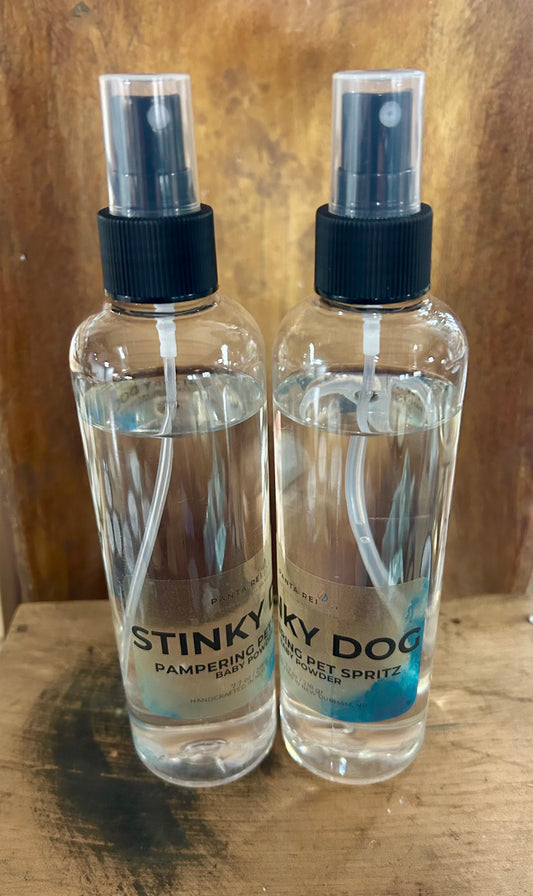 Two clear bottles of Stinky Dog pet spritz with black spray tops, shown on a wooden surface.