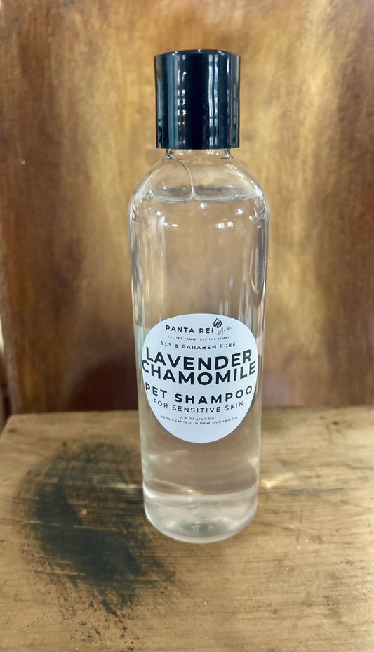 Clear bottle of Lavender Chamomile Sensitive Skin Pet Shampoo with black cap on a wooden surface.