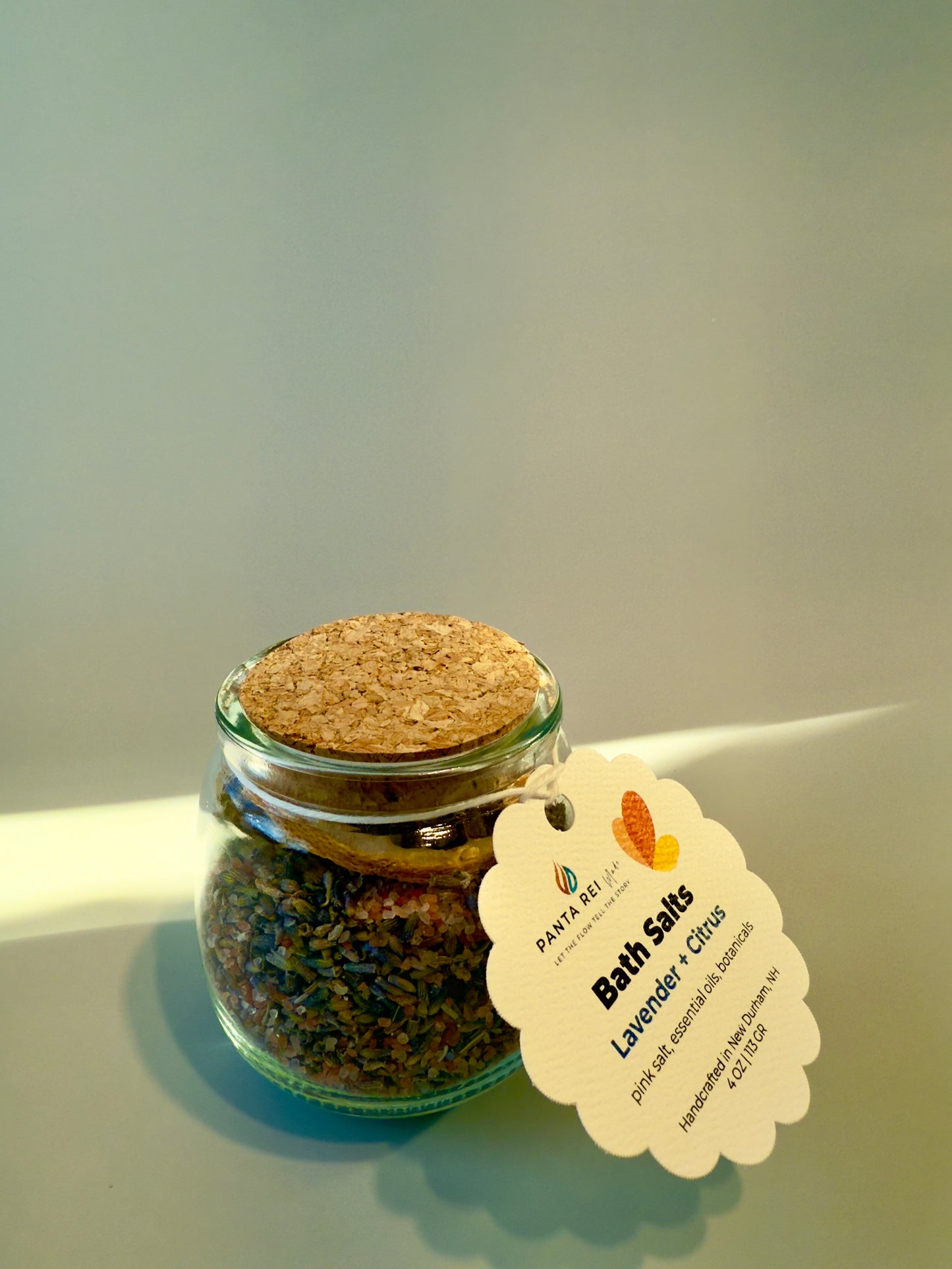 Glass jar with cork lid filled with lavender and citrus bath salts, with product tag attached.